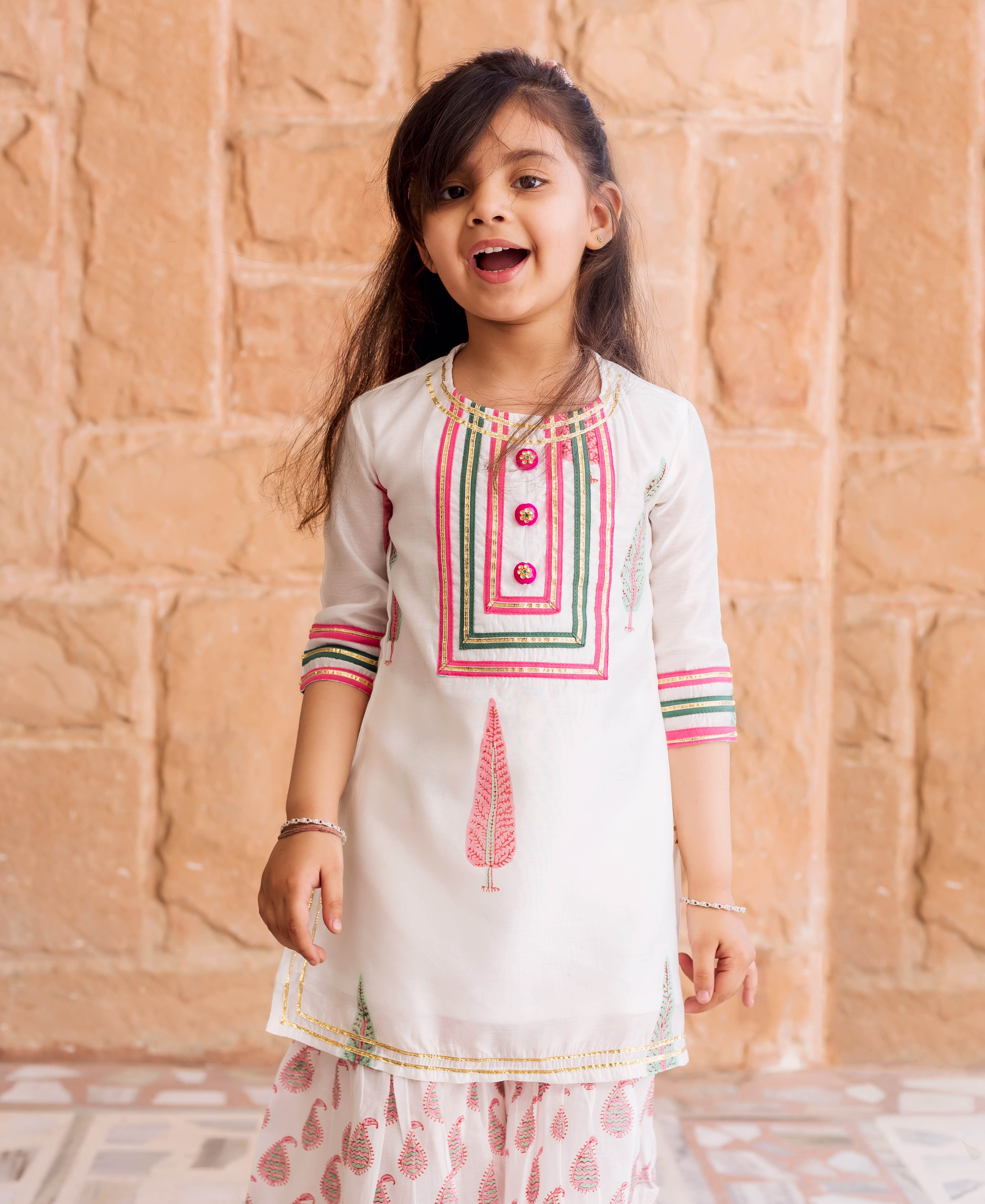 Young girl wearing a white Chanderi sharara set with pink and green block printed patterns.