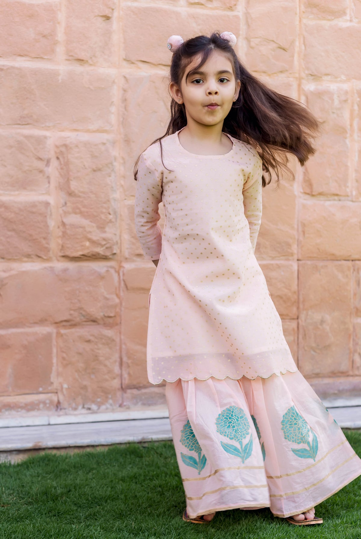 Full-length shot of a child in peach polka dot kurta and teal floral sharara set.