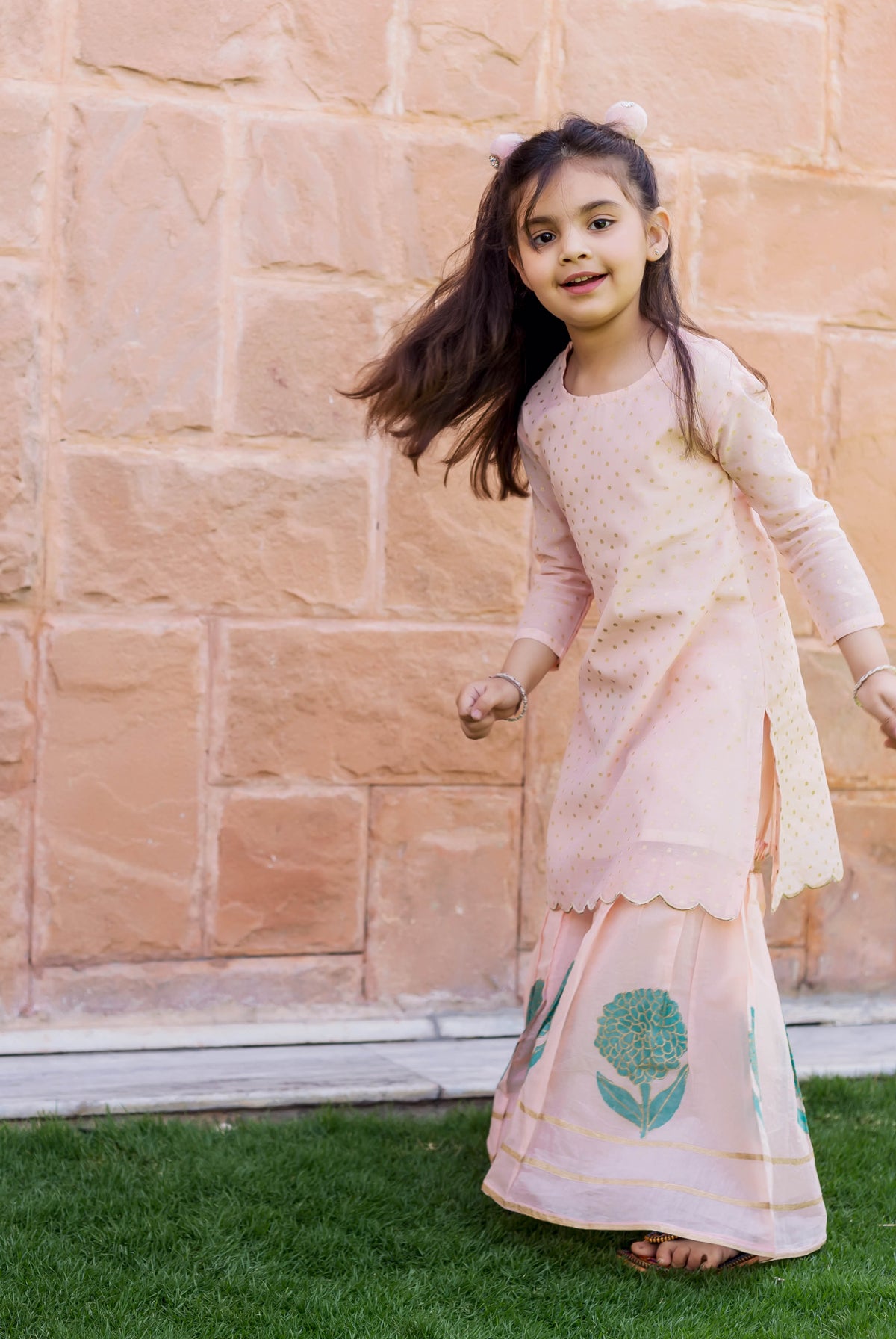 A young girl in a peach polka dot printed and embroidered sharara set.