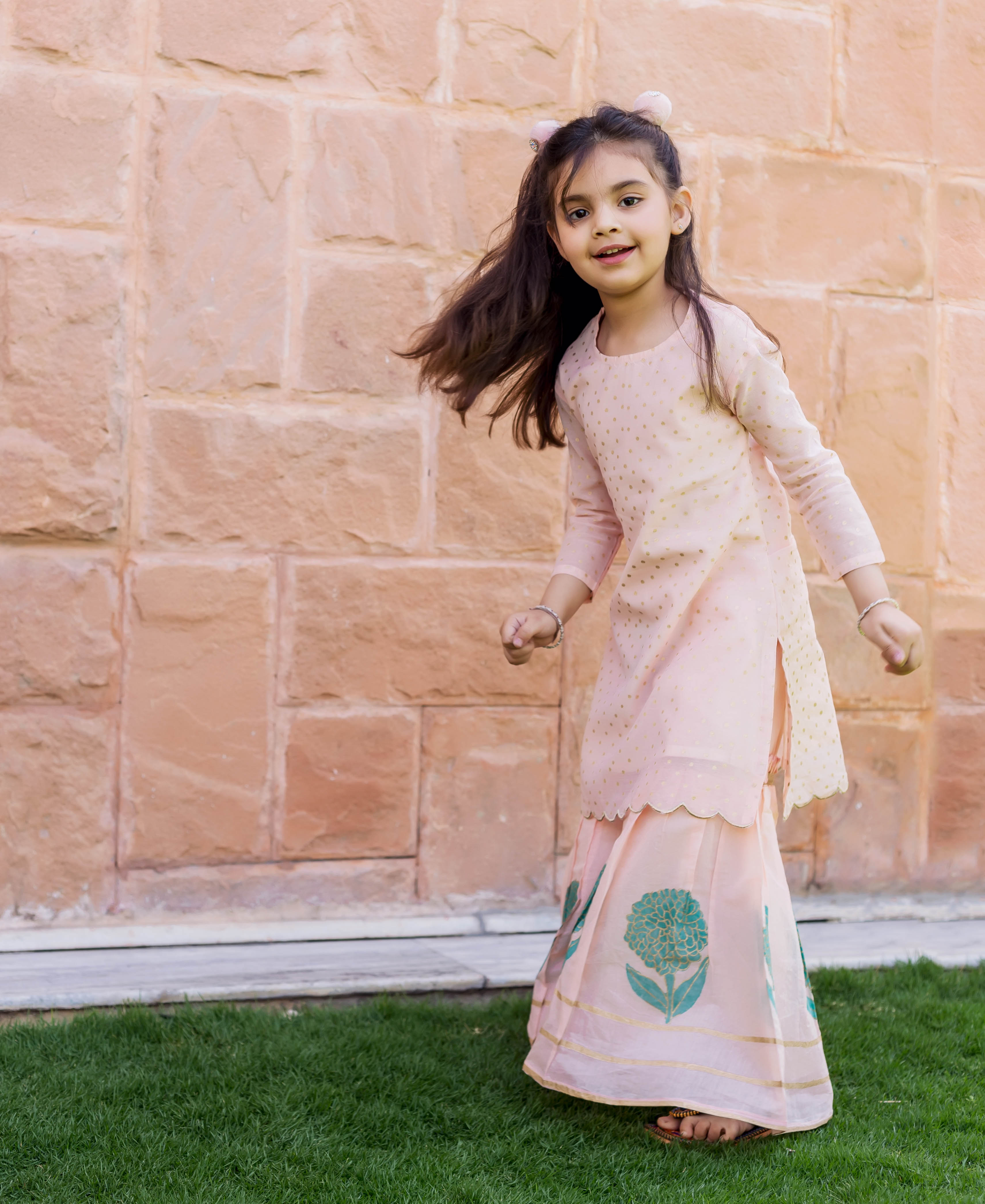A young girl in a peach polka dot printed and embroidered sharara set.
