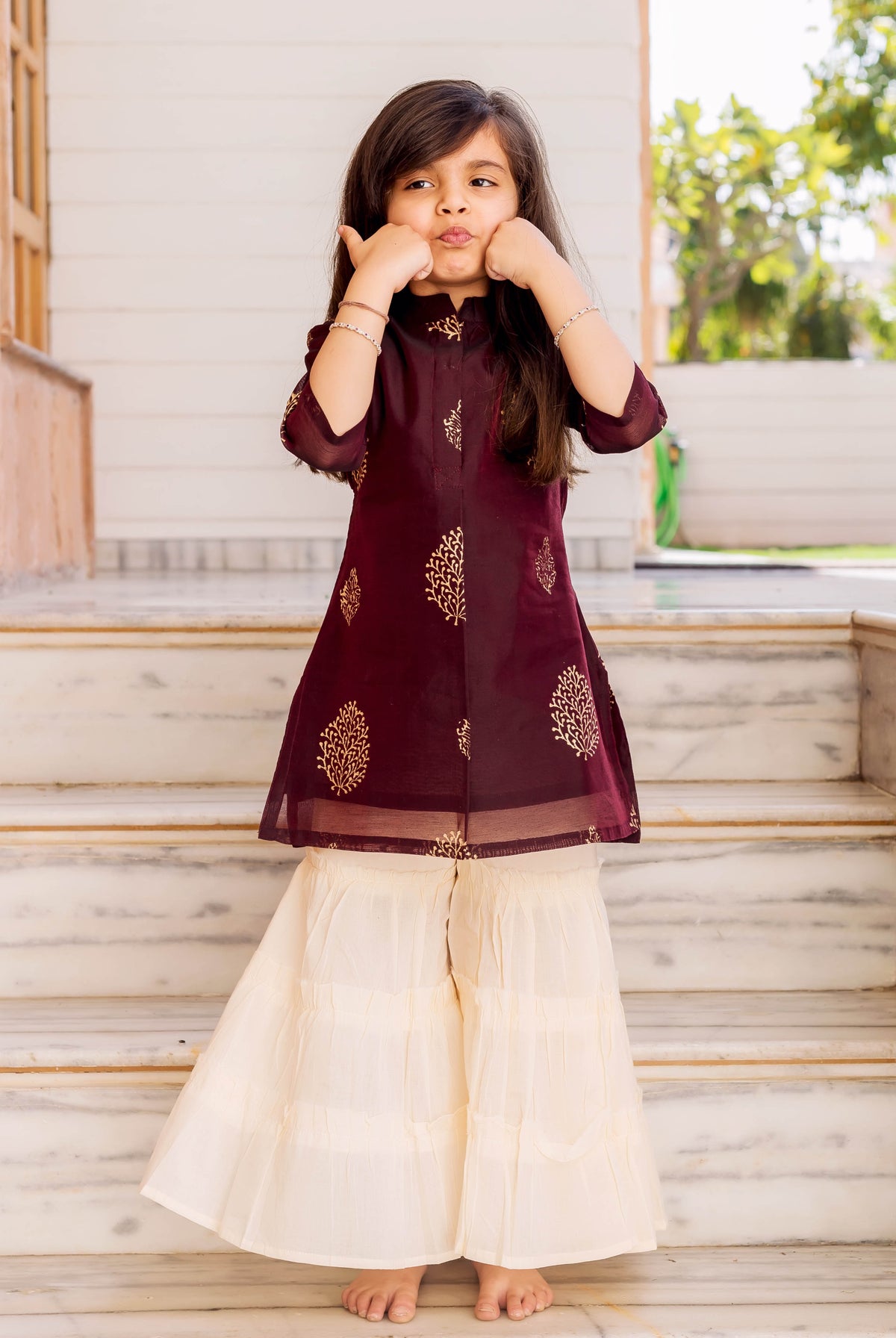 Little girl in wine gold foliage print short kurta and crème tiered sharara set.