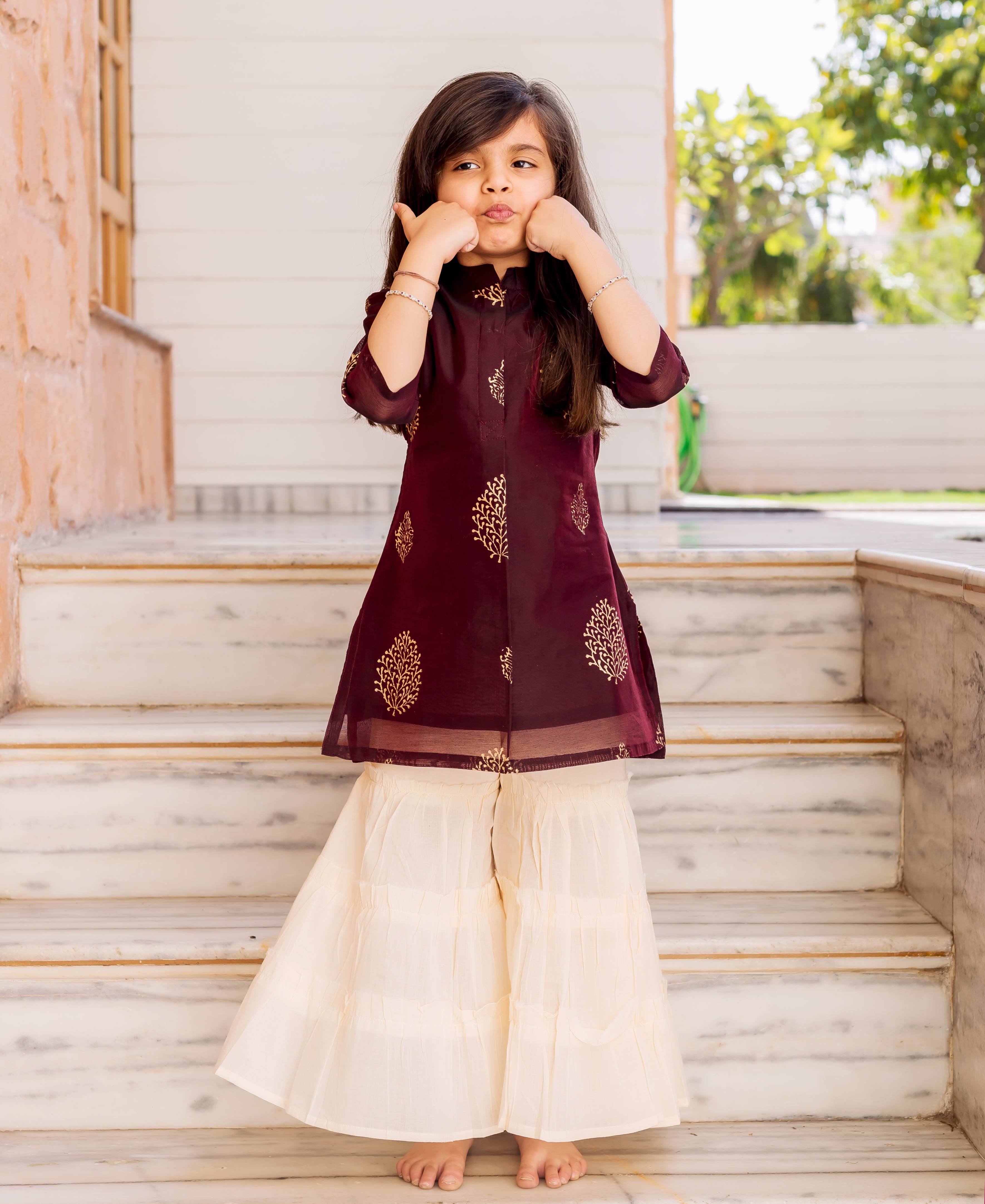 Little girl in wine gold foliage print short kurta and crème tiered sharara set.