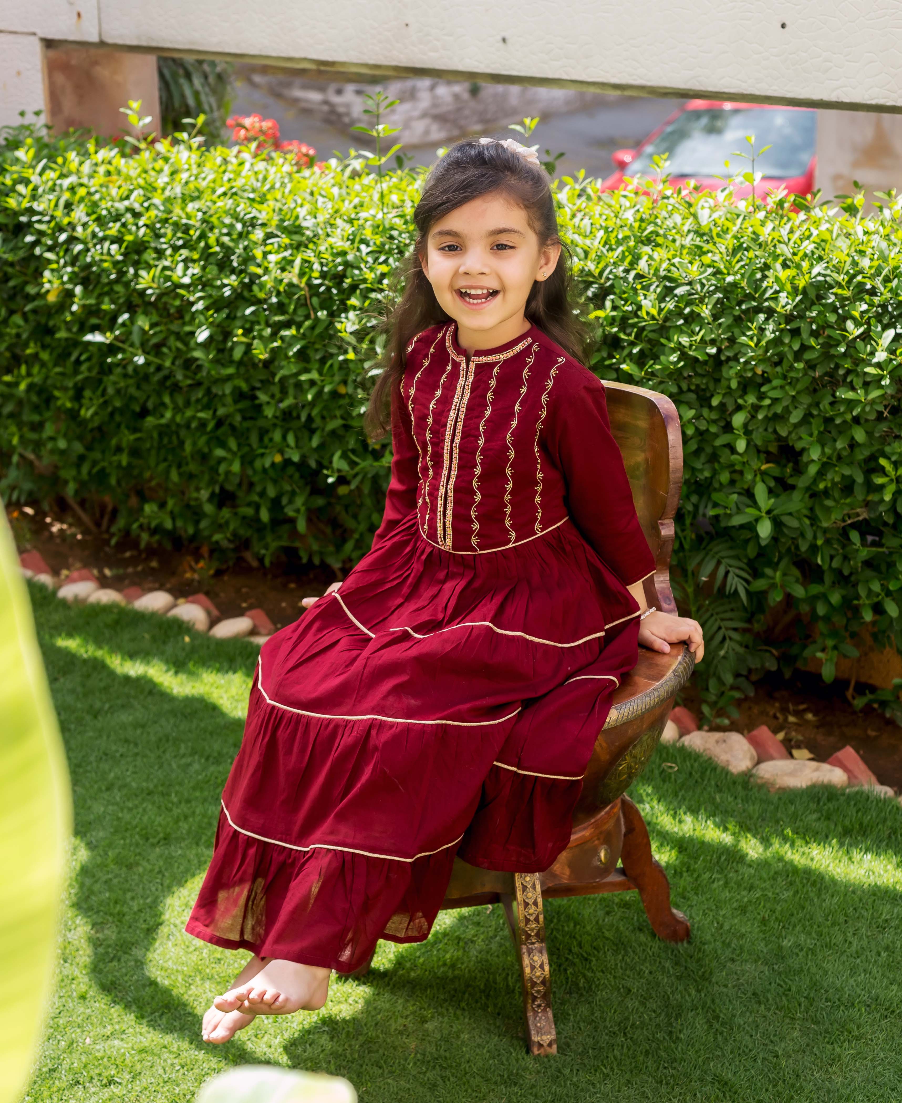 Smiling girl models maroon tiered dress with gold hand embroidery on bodice and tiers.