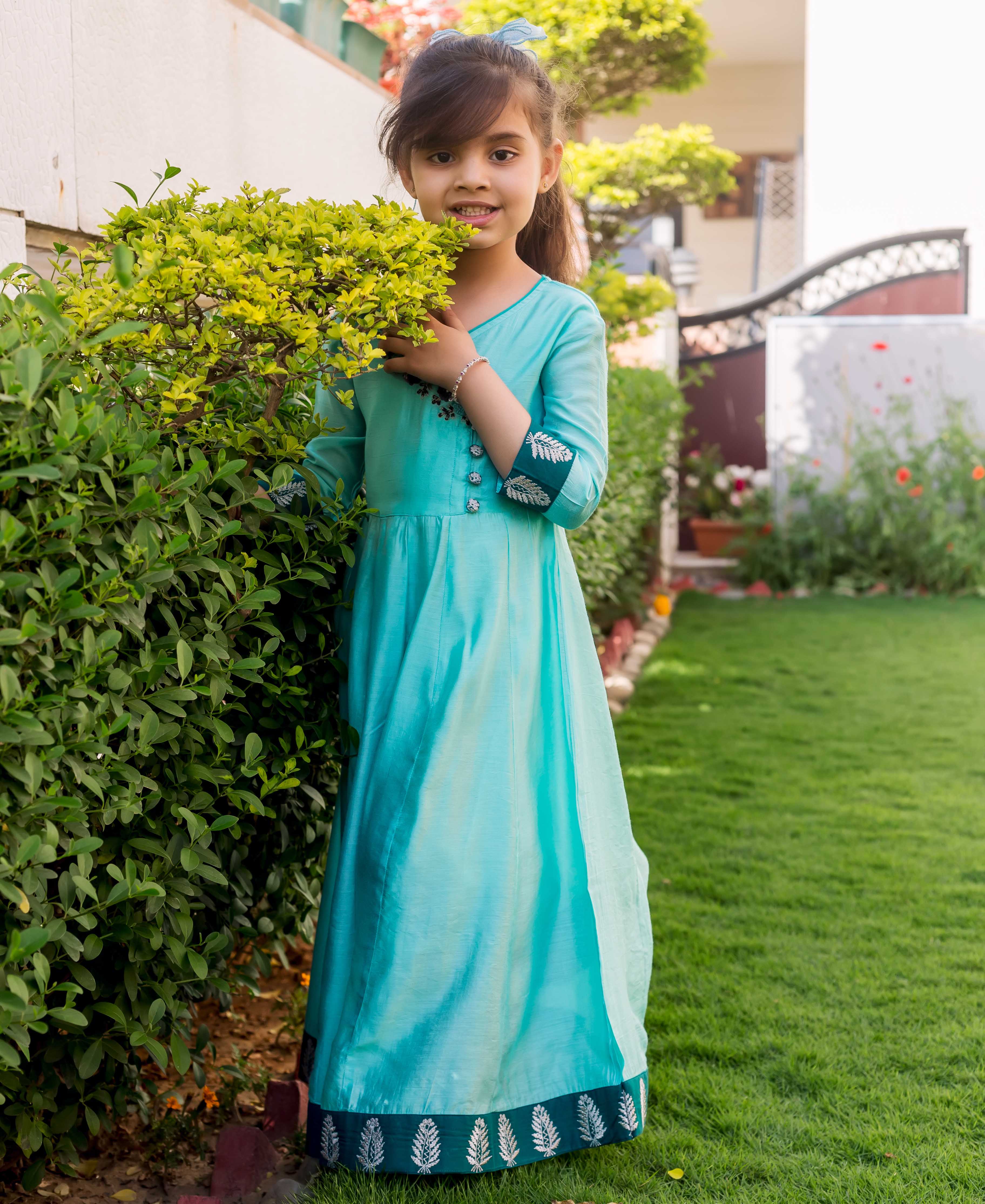 Young girl wears a full-length mint green Angrakha dress with embroidered details and printed border.