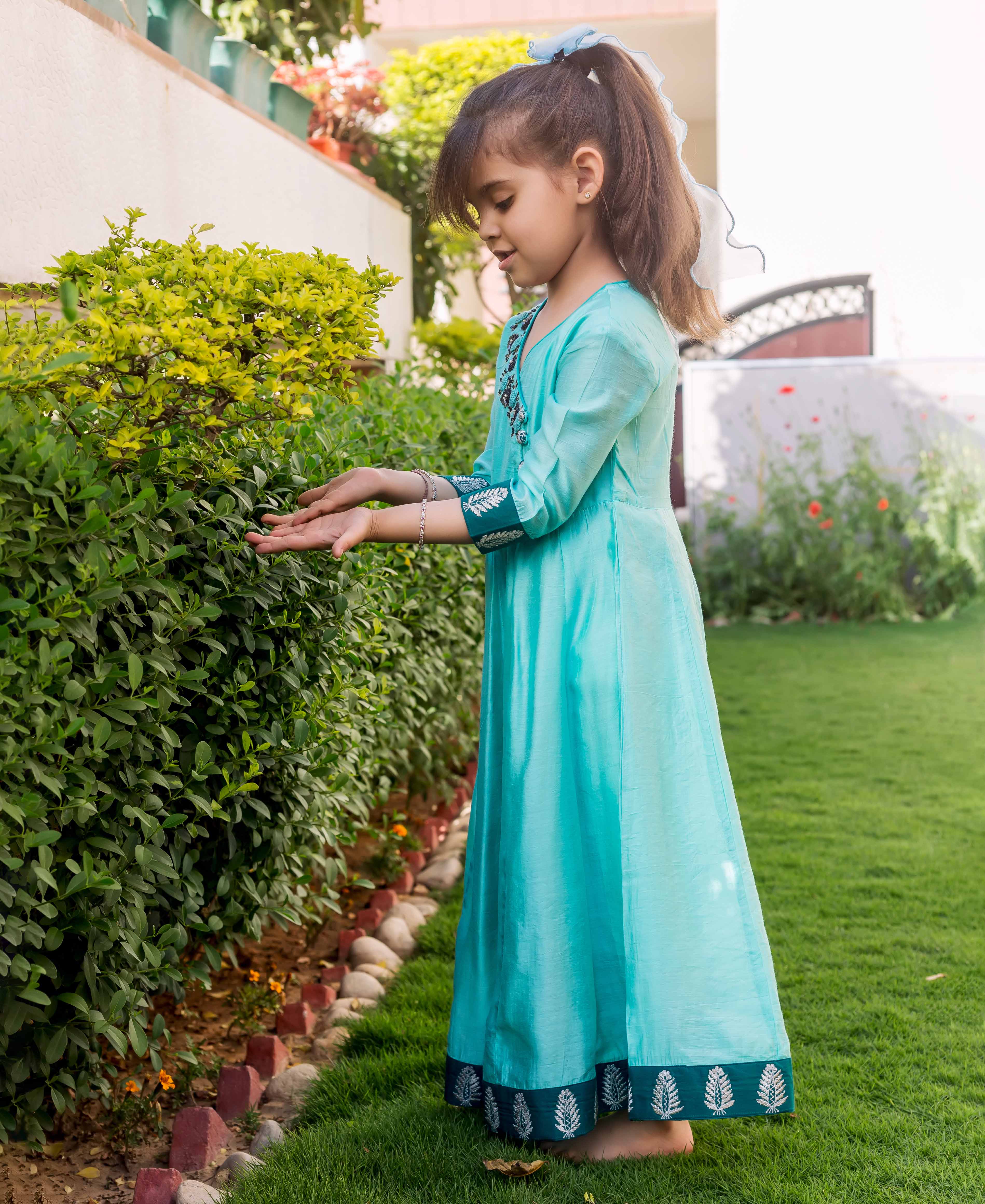 Side view of young girl in mint green hand embroidered Angrakha dress with leaf print.