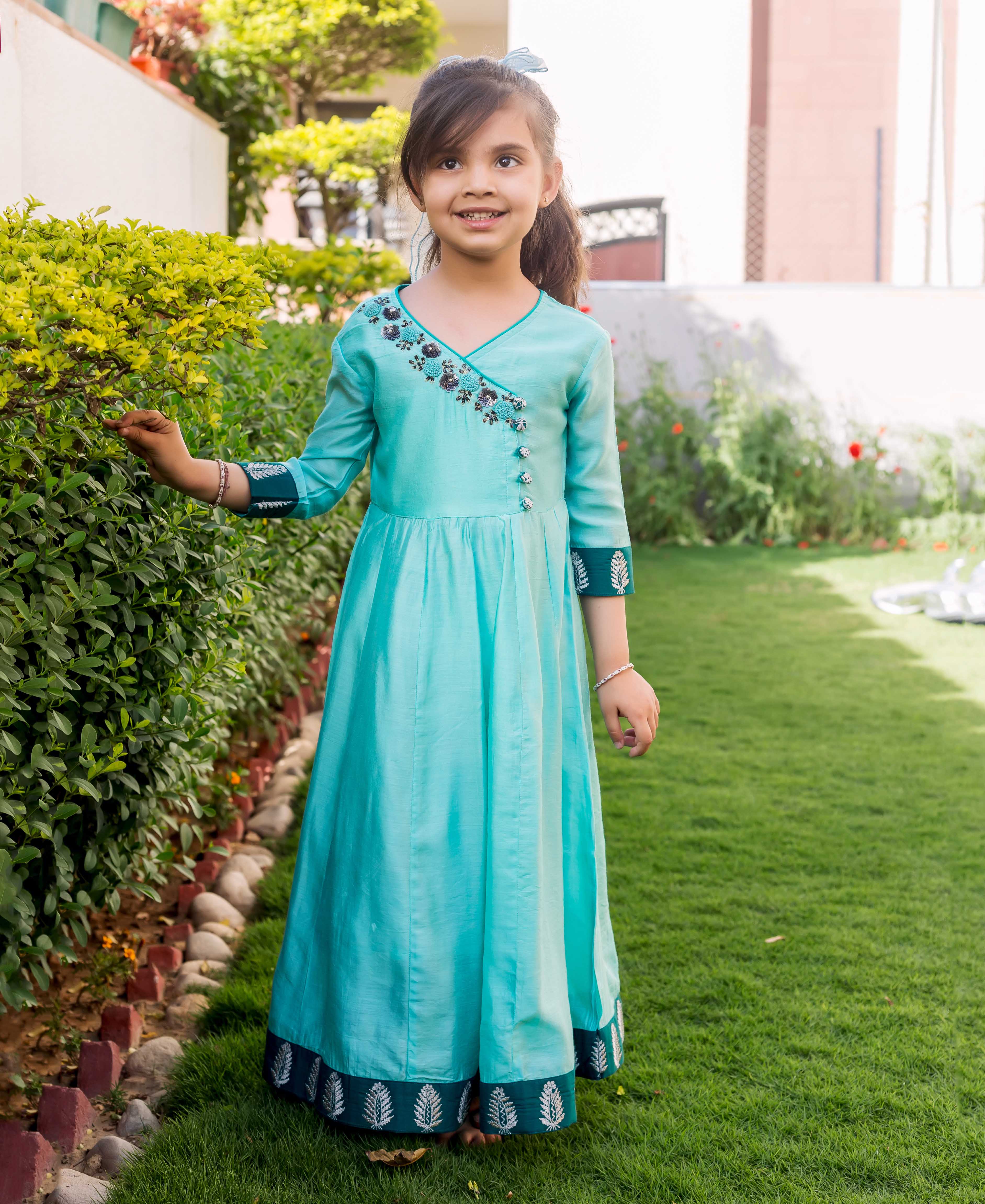 Young girl stands wearing a full-length mint green Angrakha dress with embroidered neckline and printed borders.