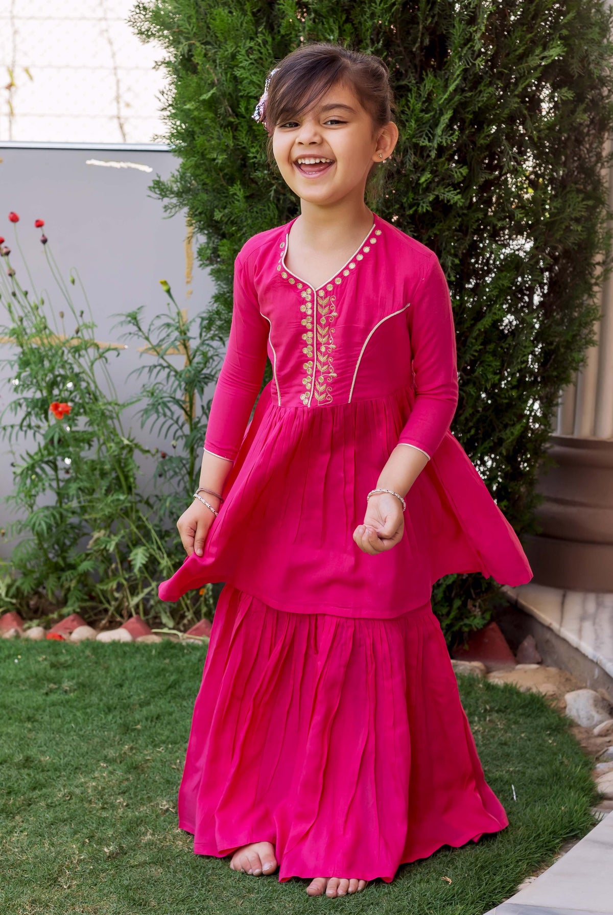 Vibrant pink hand-embroidered sharara set with gold details on a young girl outdoors.