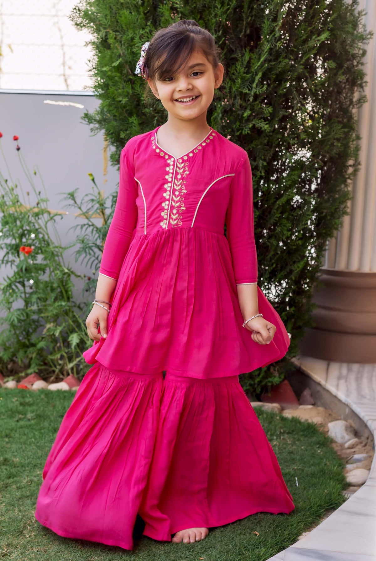 A young girl in a pink sharara set with gold embroidery.