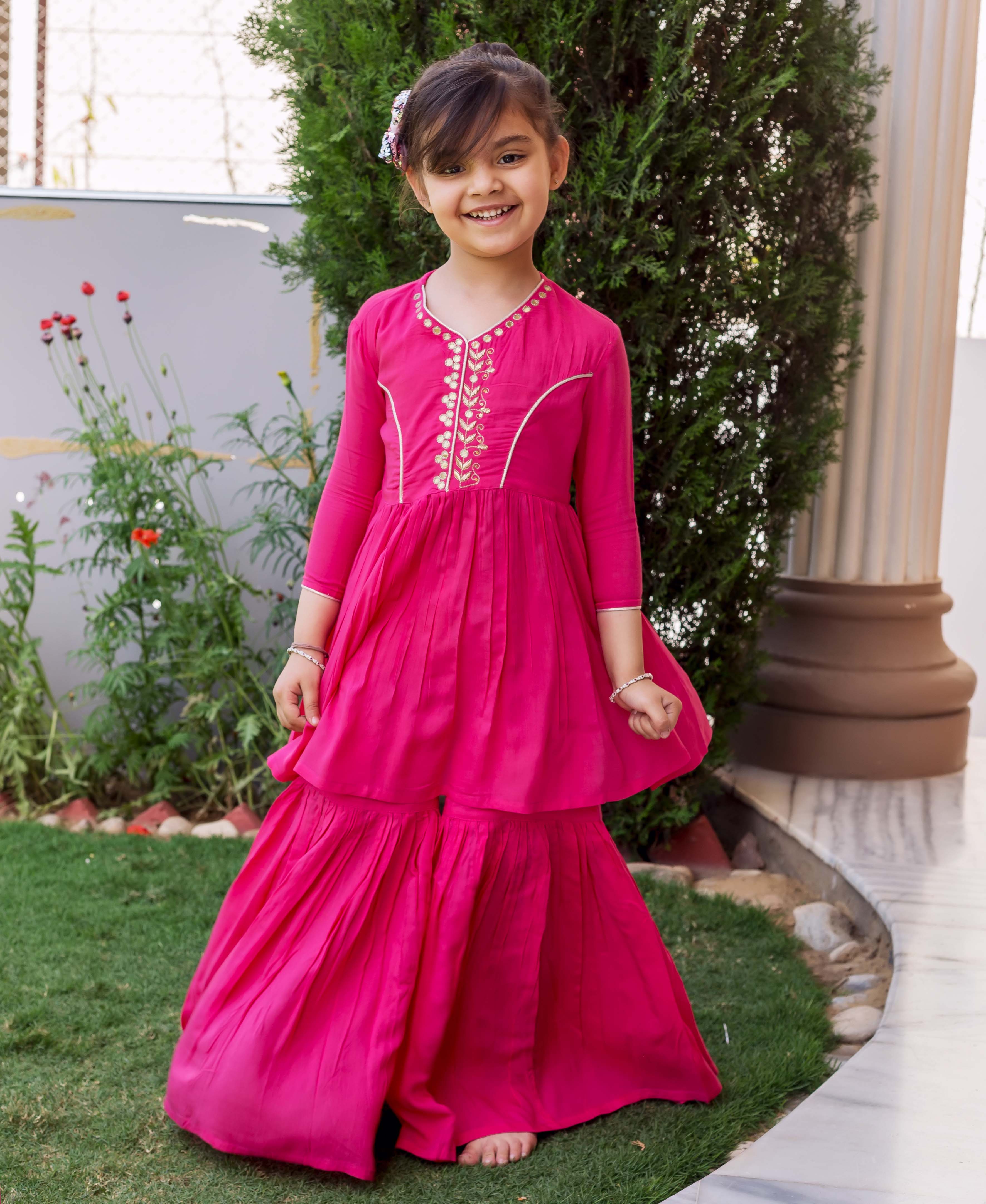 A young girl in a pink sharara set with gold embroidery.