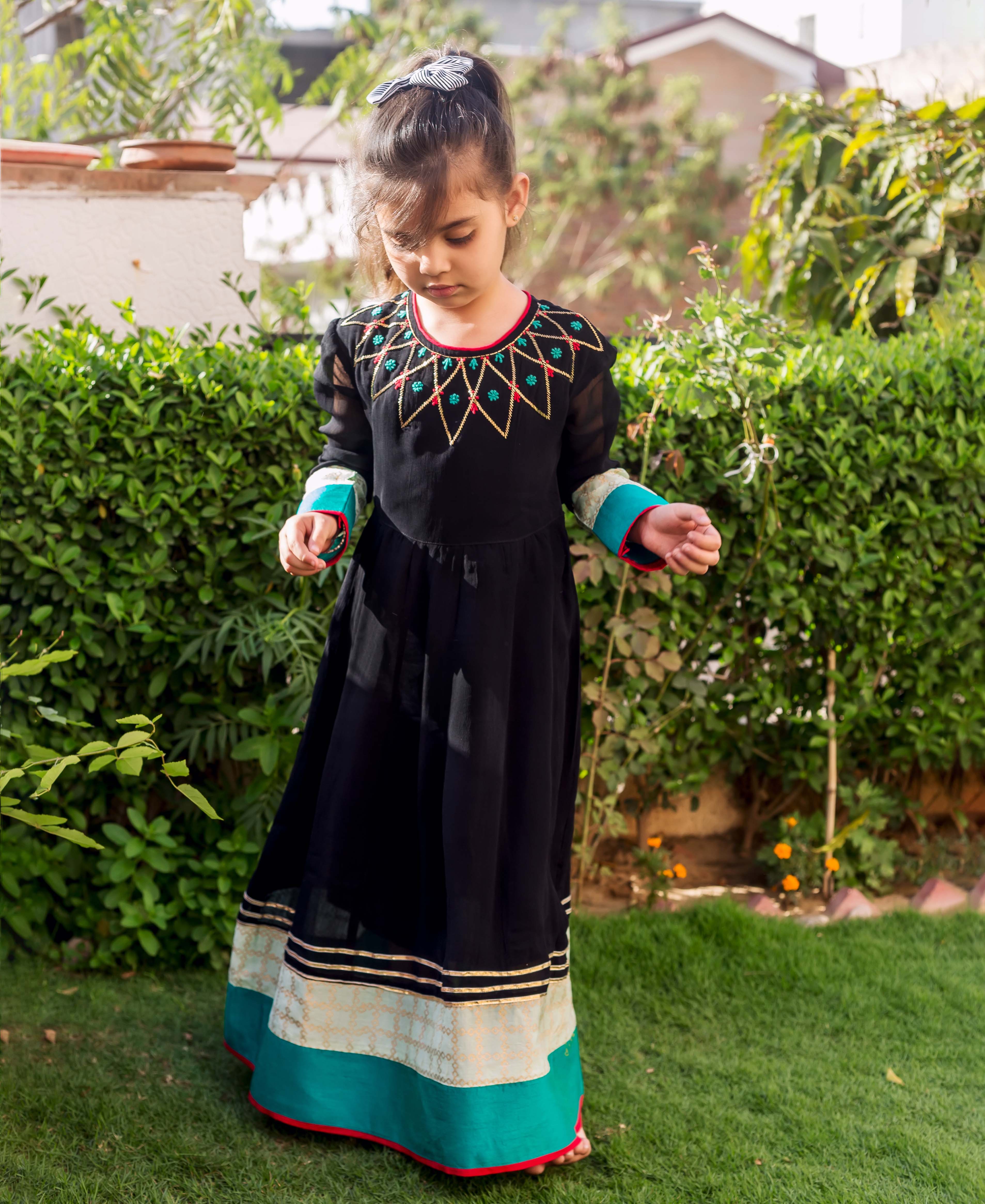 Front full look of young girl in black Anarkali with embroidered yoke and patterned teal hem.