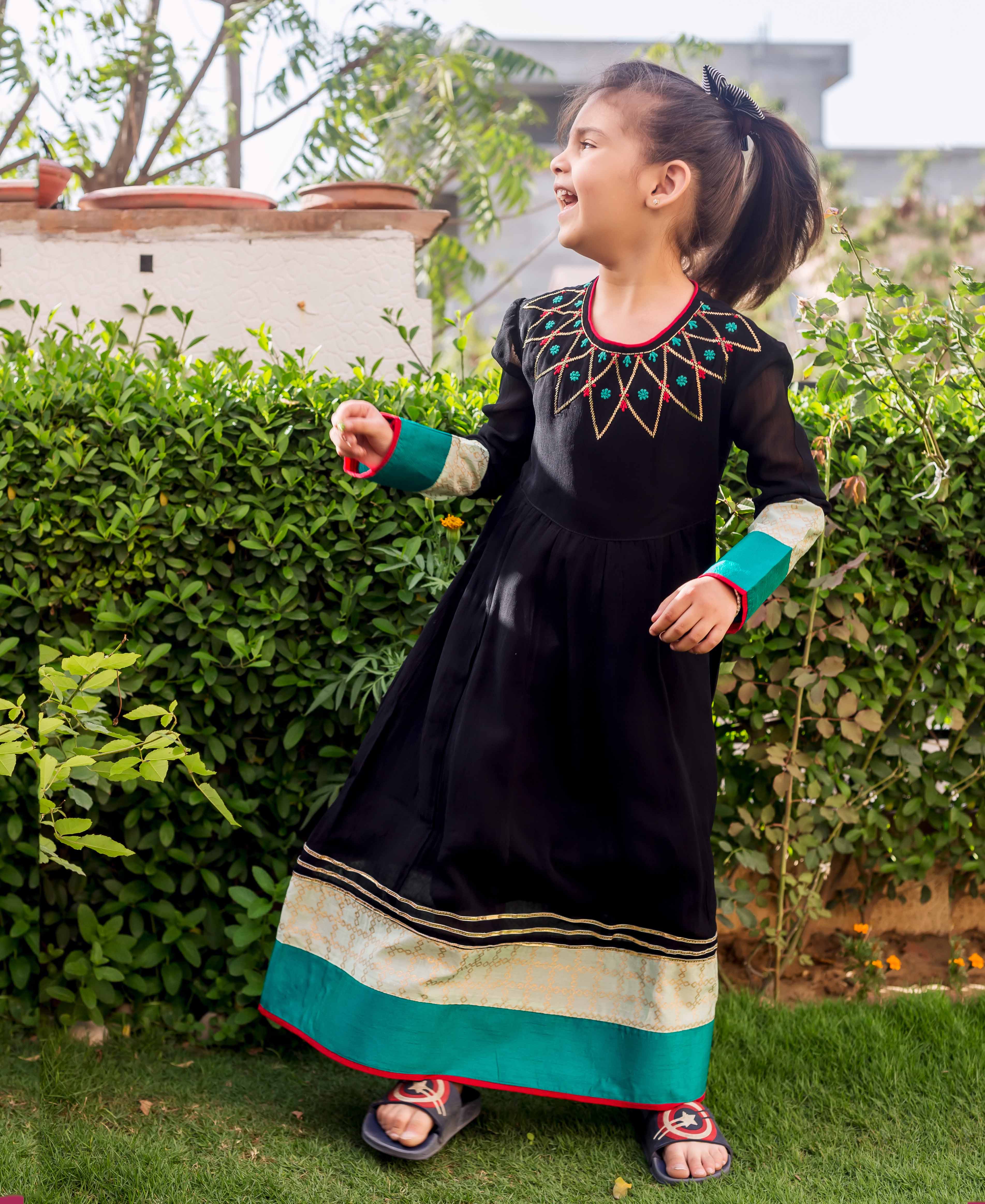 Black anarkali dress on model with embroidered yoke, patterned cuffs, and gold-teal border.