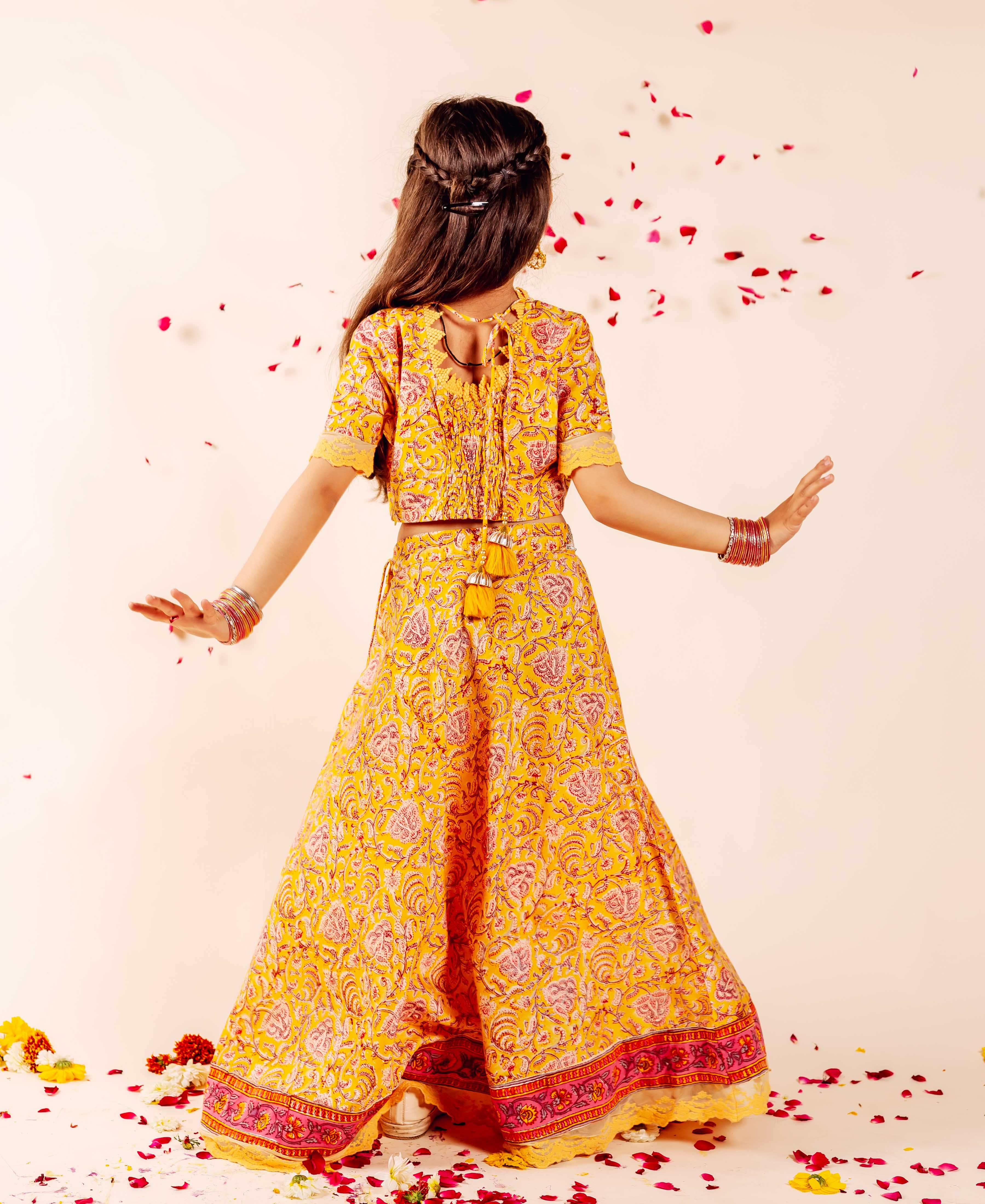 Back view of girl in yellow Farida Lehenga Set, pink ethnic floral print skirt and crop top.