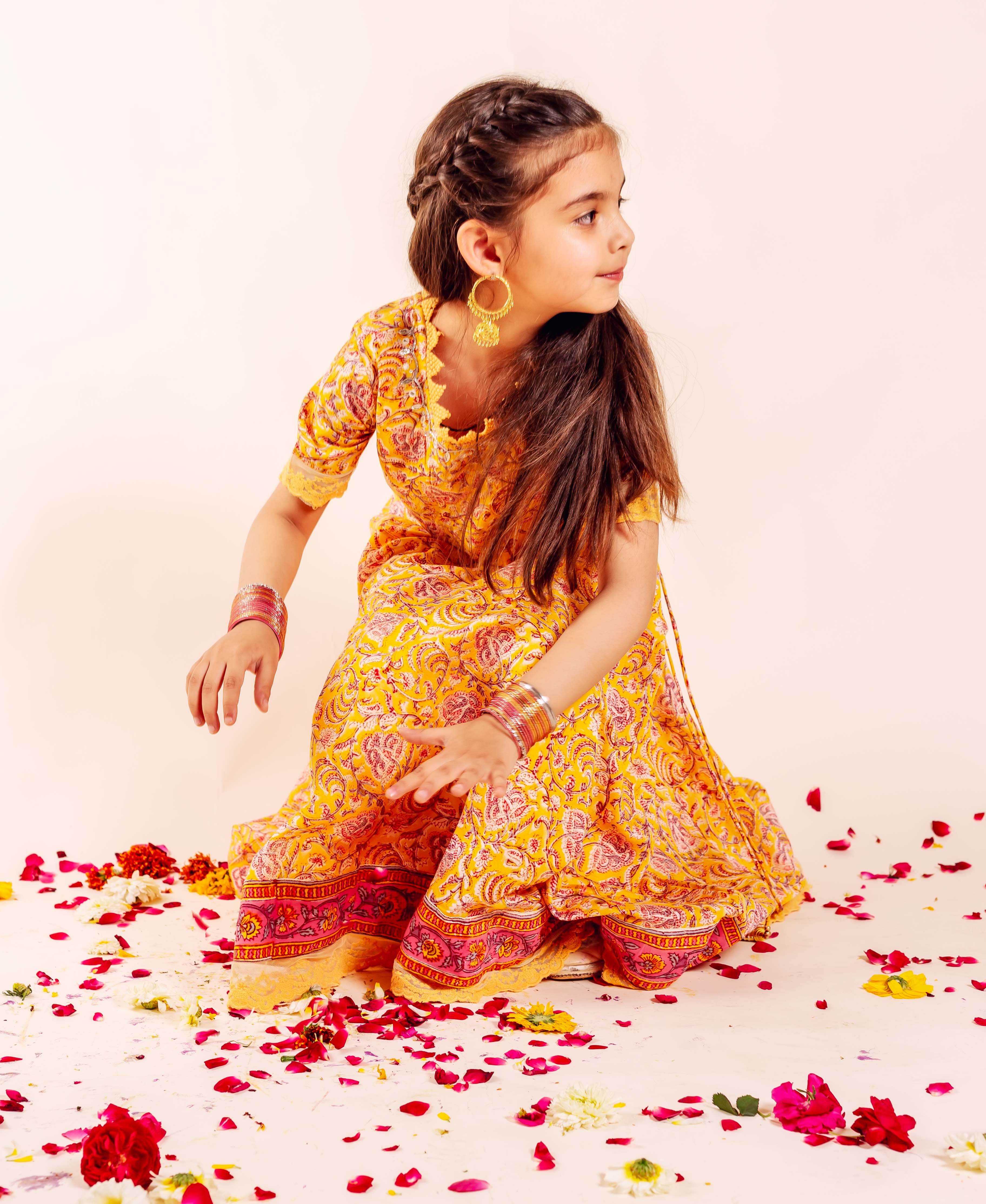 Child model wearing yellow hand-block-printed lehenga set with floral and paisley patterns.