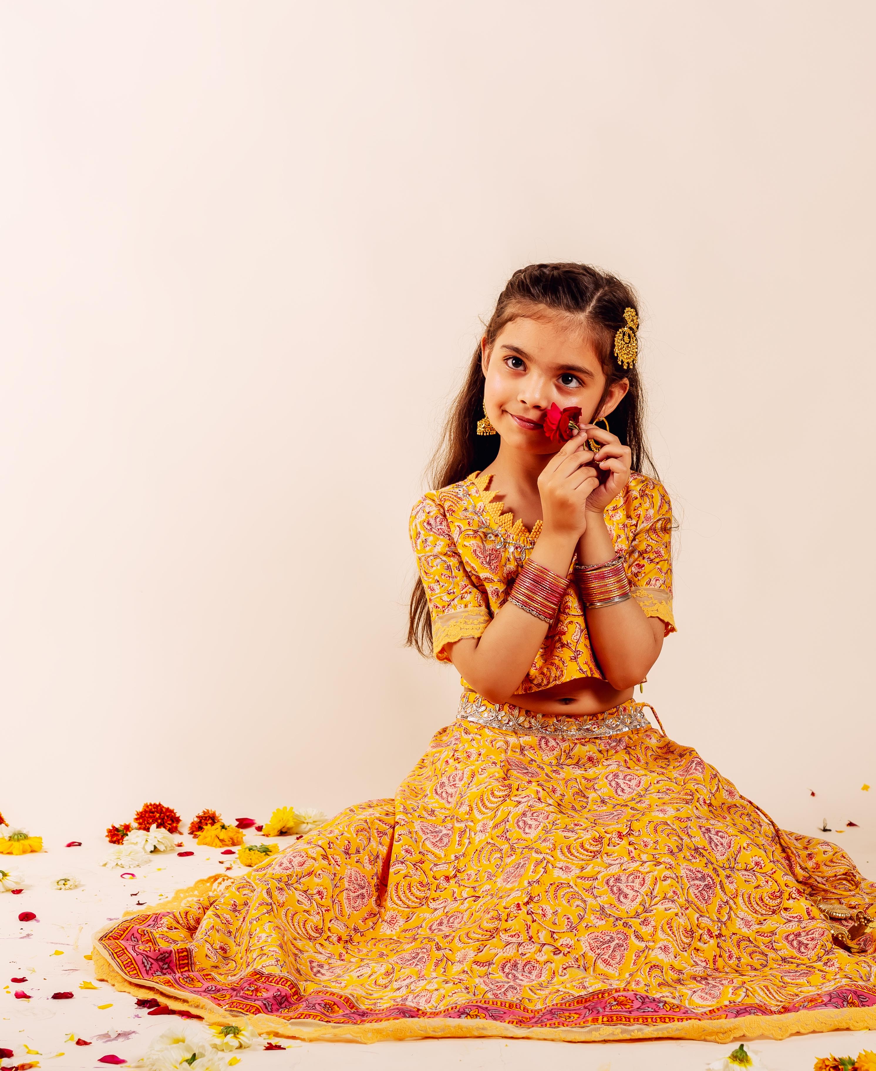 Young girl sitting, wearing a yellow hand-block printed ethnic Farida lehenga set with floral details.