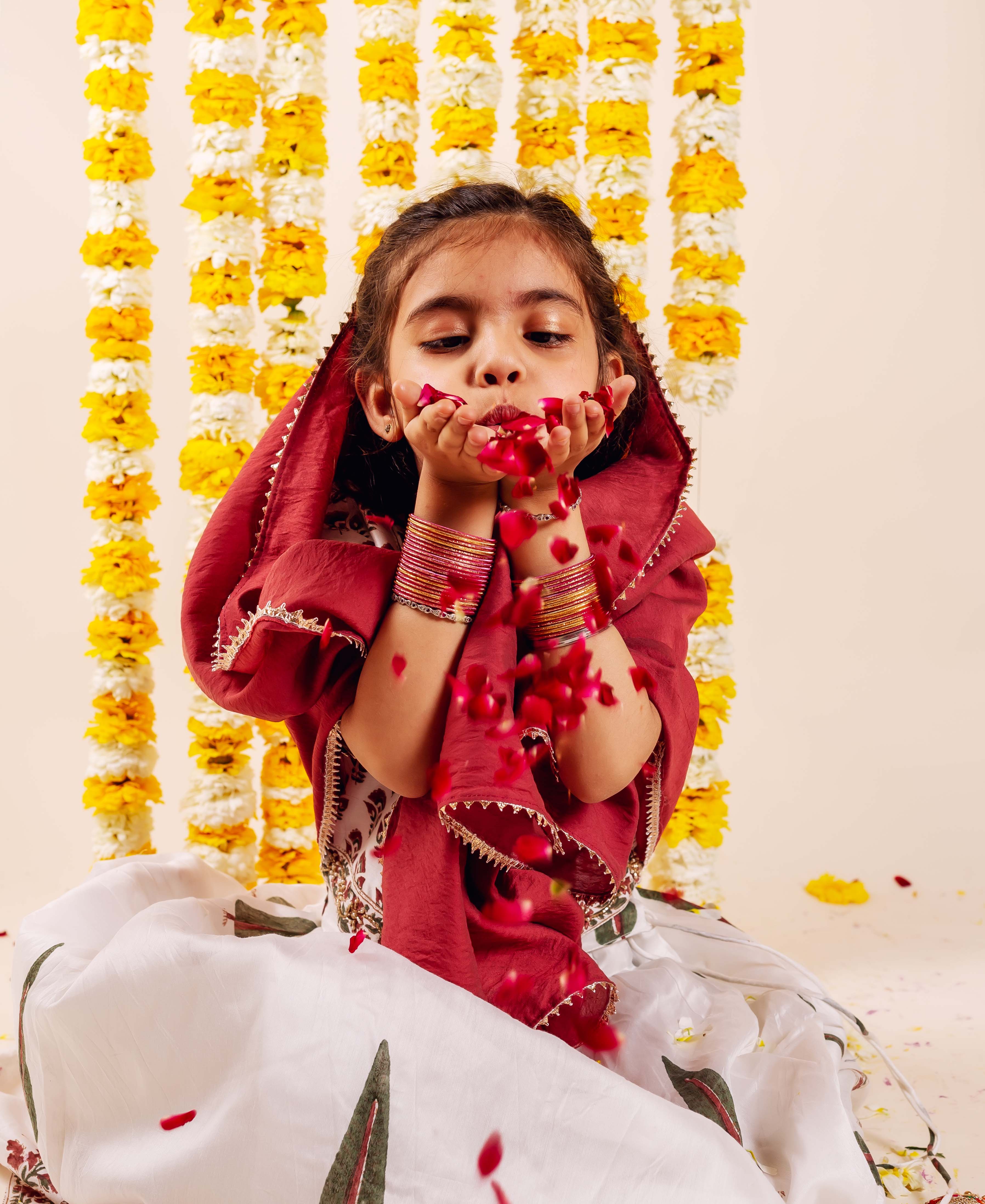 Baby girl in white hand-block printed ethnic lehenga set with maroon dupatta.