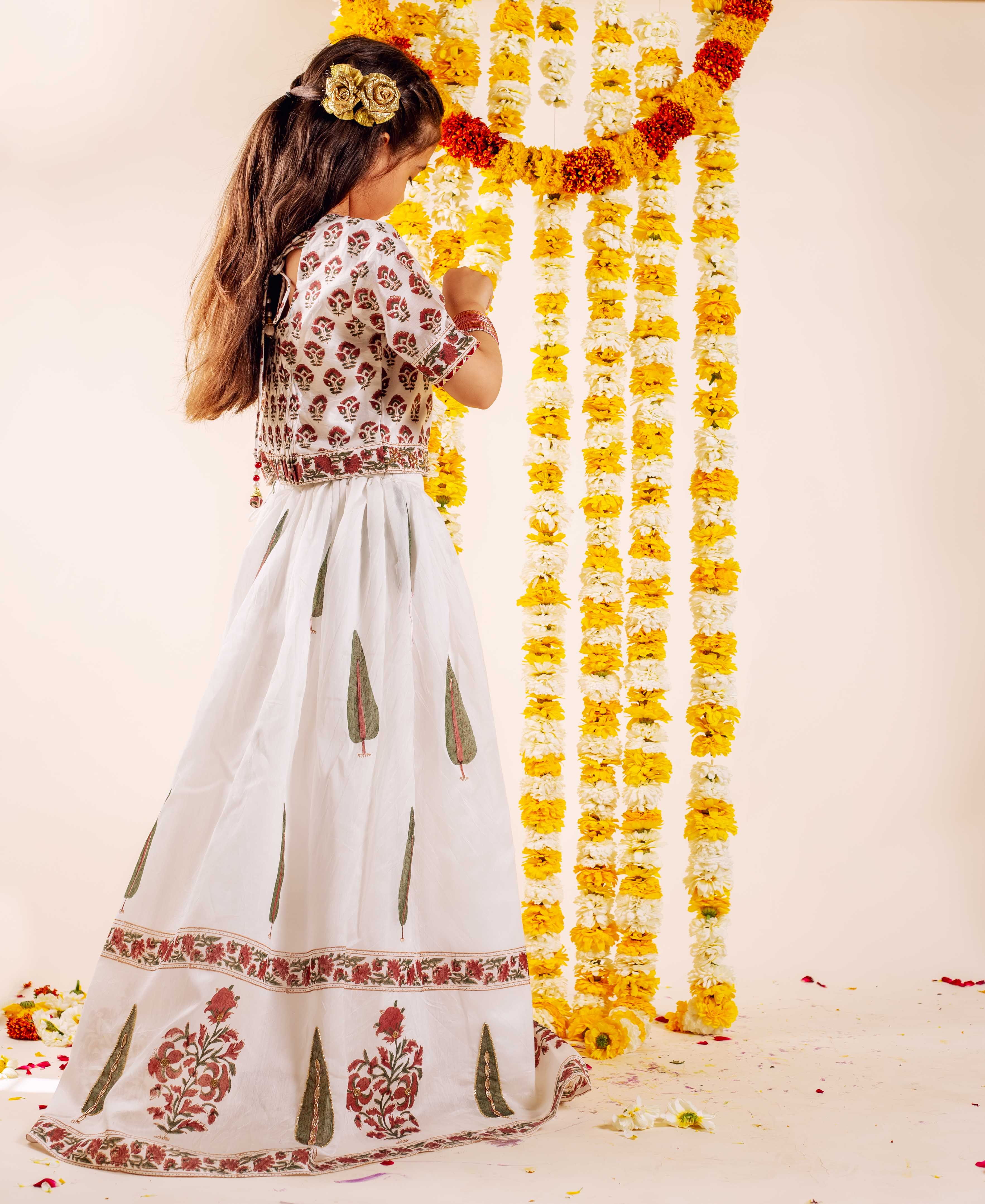 Young girl's back, white hand-block-printed ethnic lehenga set, red floral, green leaves.