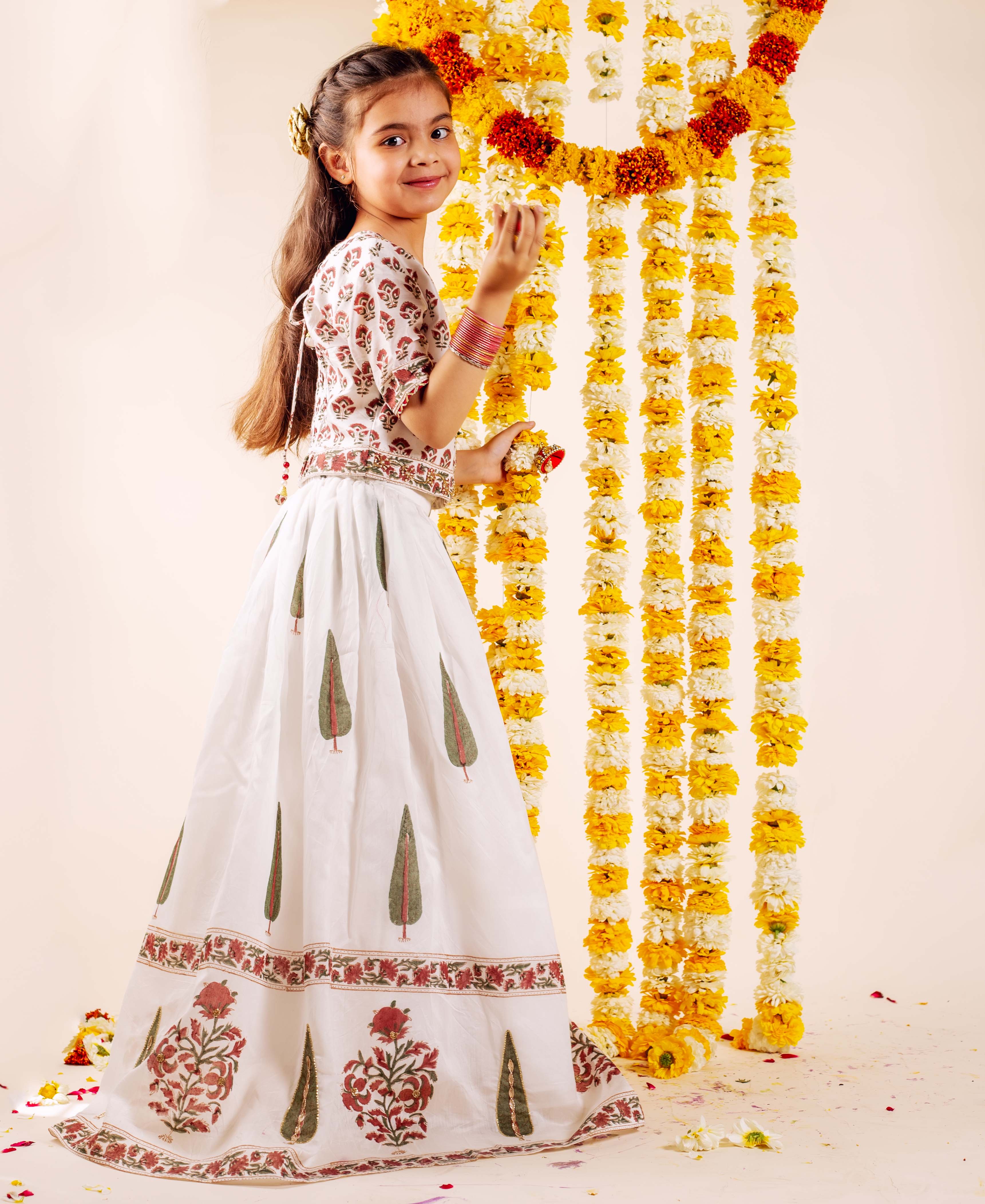 Young girl wearing white hand-block-printed lehenga set with red and green floral designs.