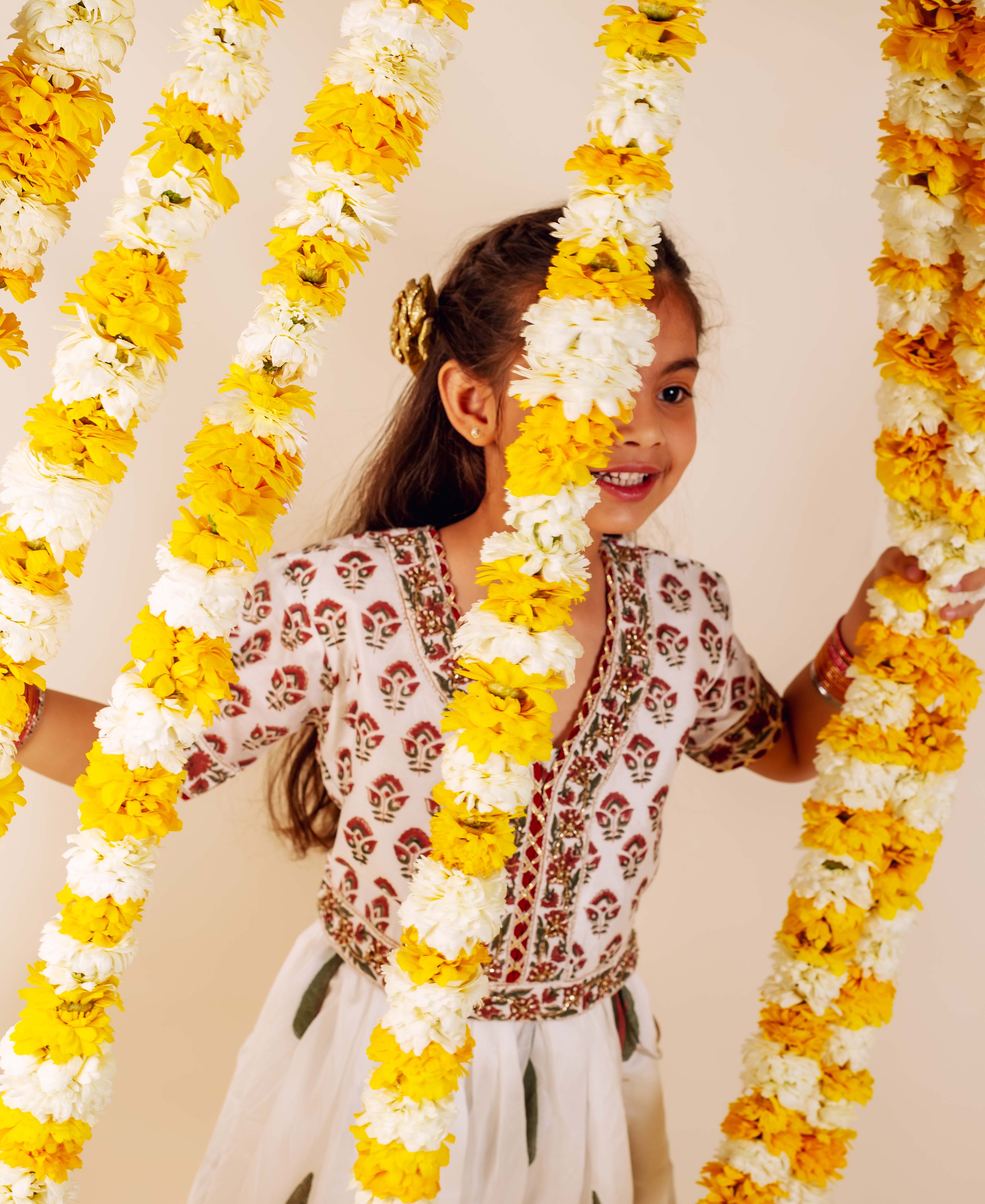 Young girl in white embroidered lehenga set with red, green hand-block-printed patterns.