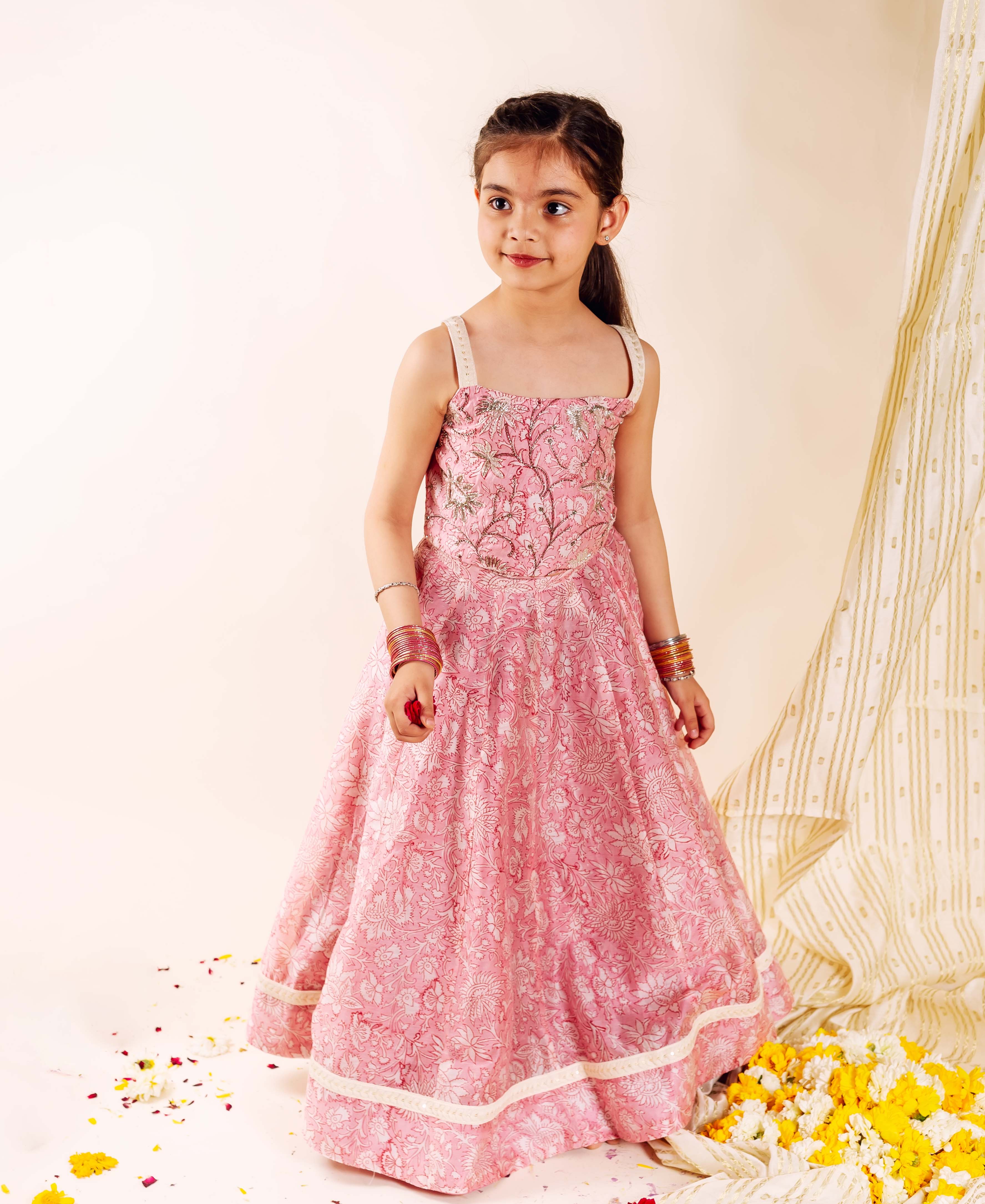 Young girl models a vibrant pink hand-block-printed lehenga set featuring intricate floral patterns.