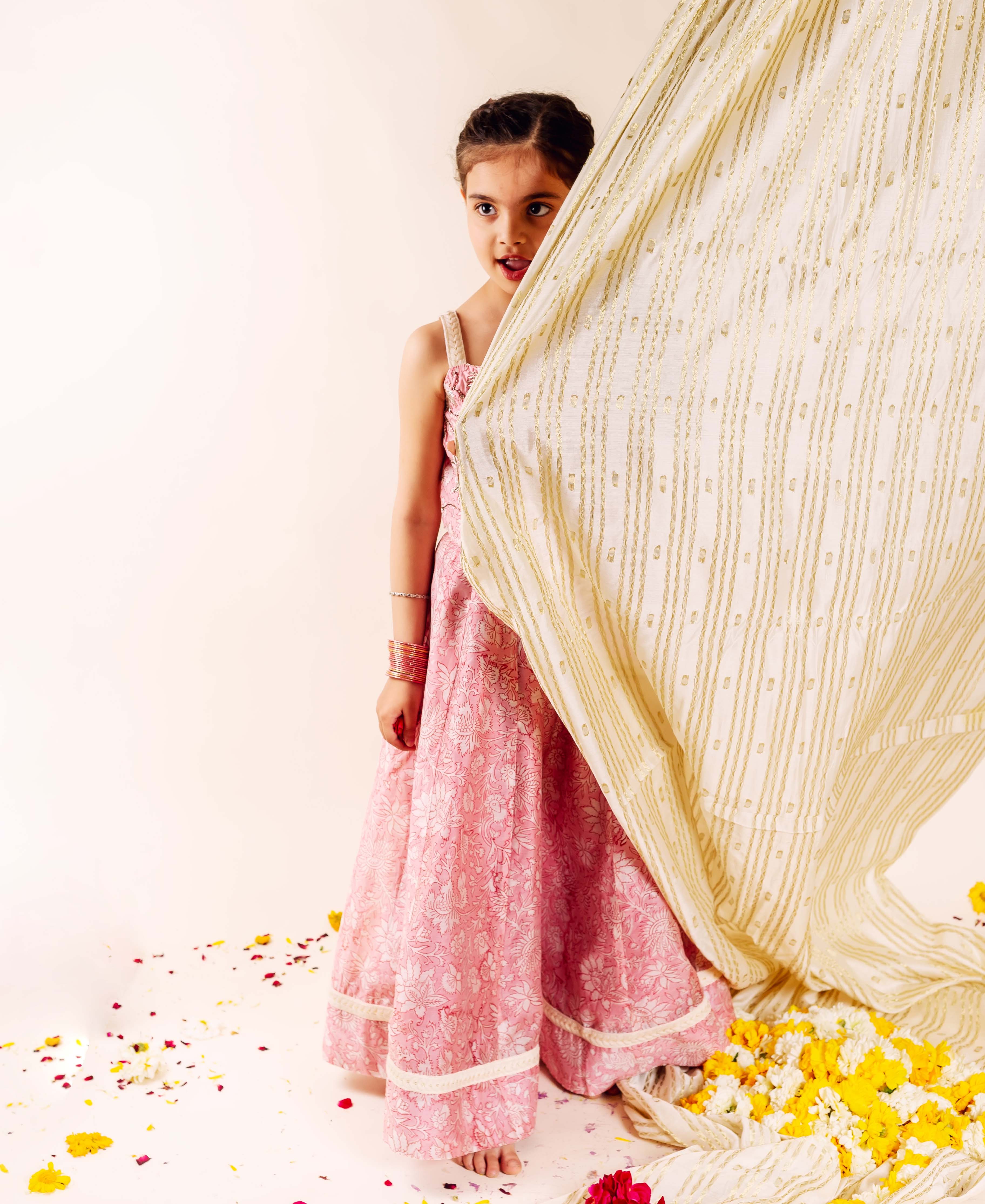 Young girl in a pink floral hand-block printed lehenga and gold-embroidered cream dupatta.