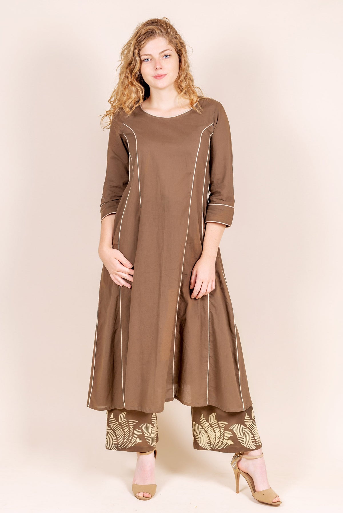 Model wears a brown A-line kurta with white piping and hand-block-printed beige palazzo pants.