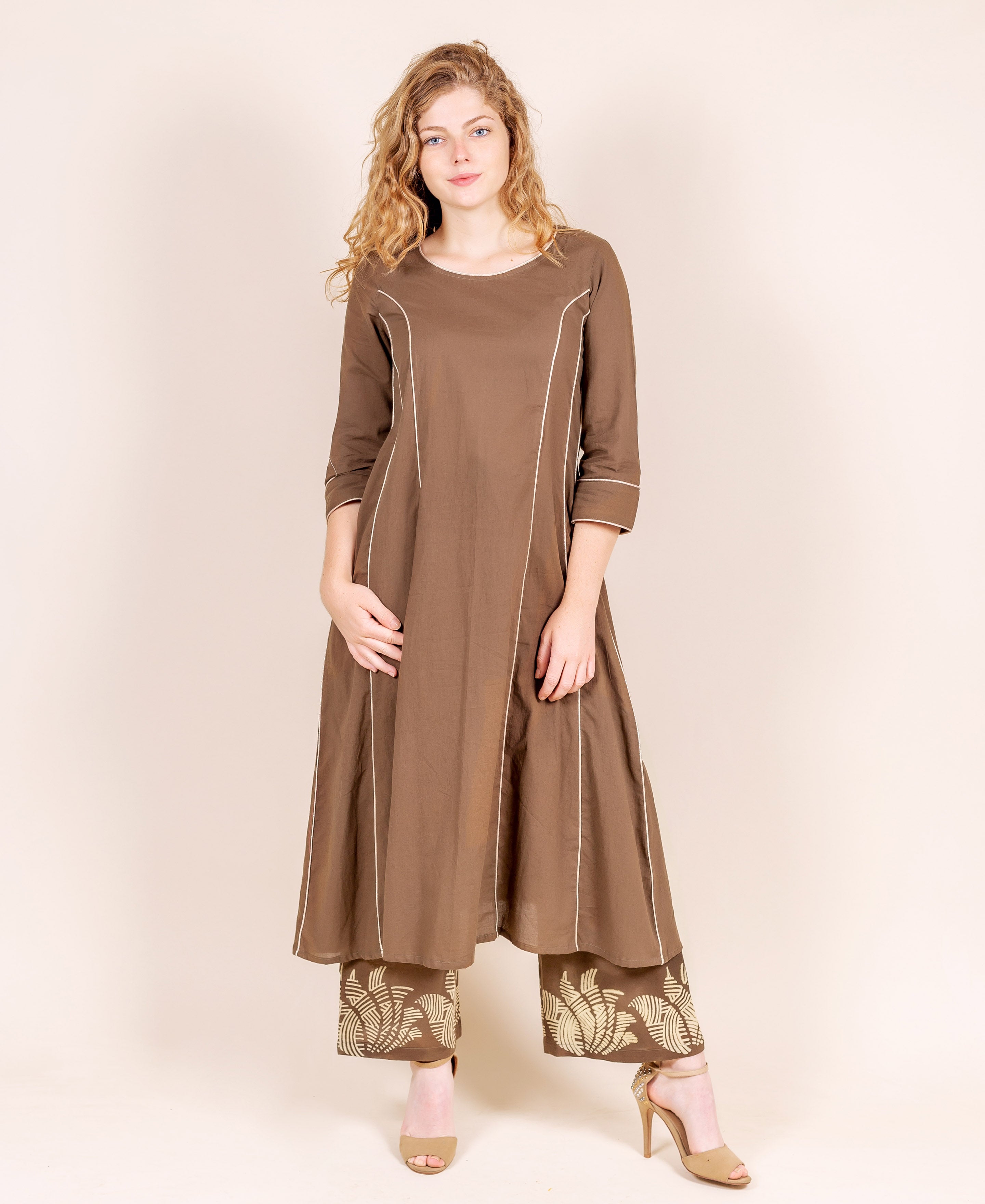 Model wears a brown A-line kurta with white piping and hand-block-printed beige palazzo pants.