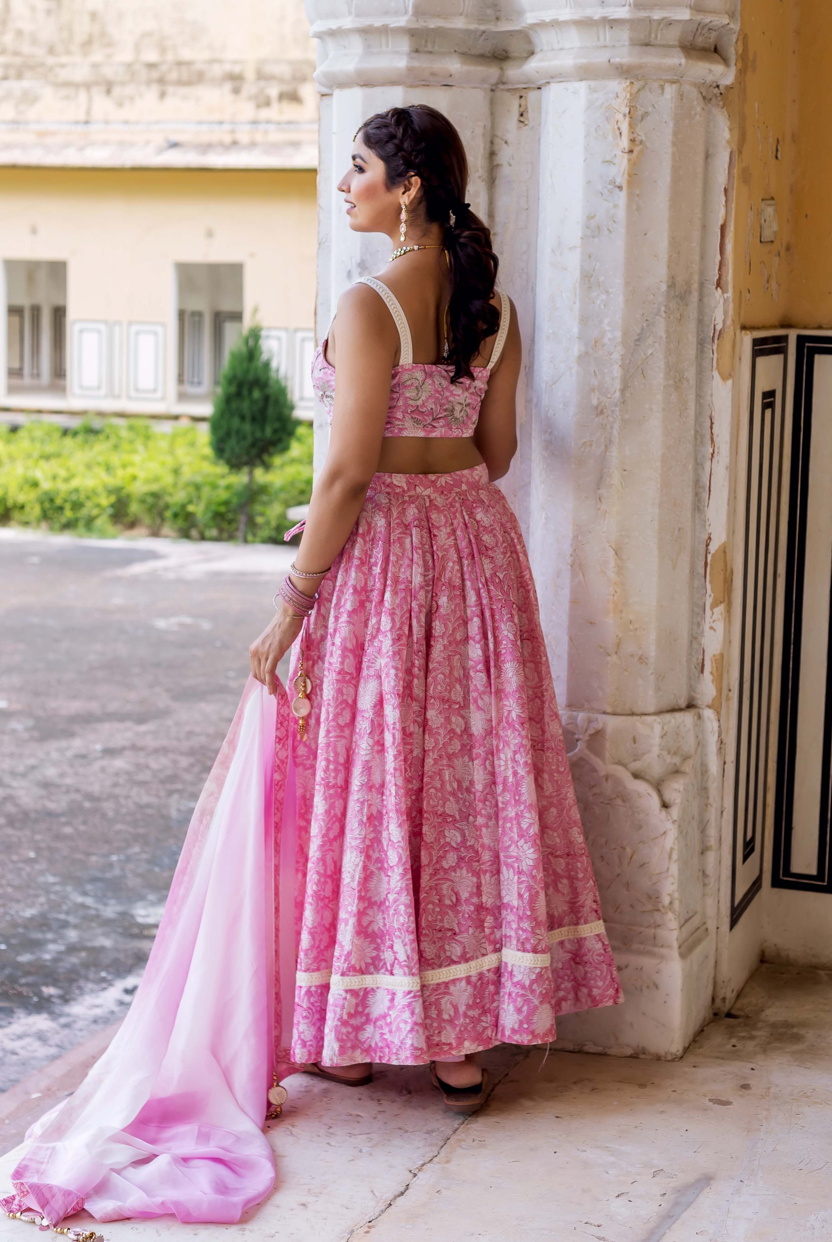 Rear view of model in pink hand-block-printed floral lehenga set with flowing dupatta.