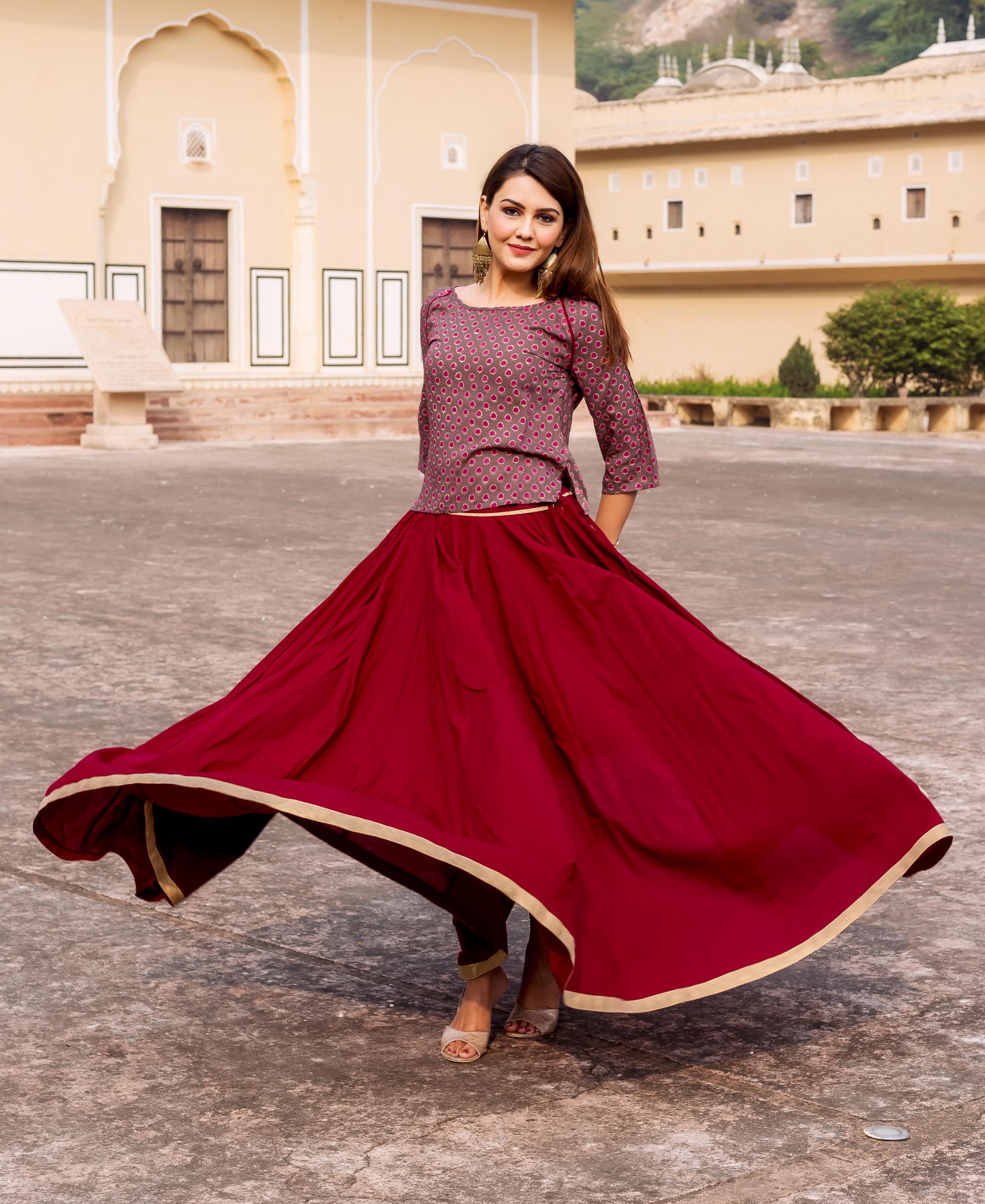 Model twirling in a maroon skirt with gold gota trim and printed ethnic top.