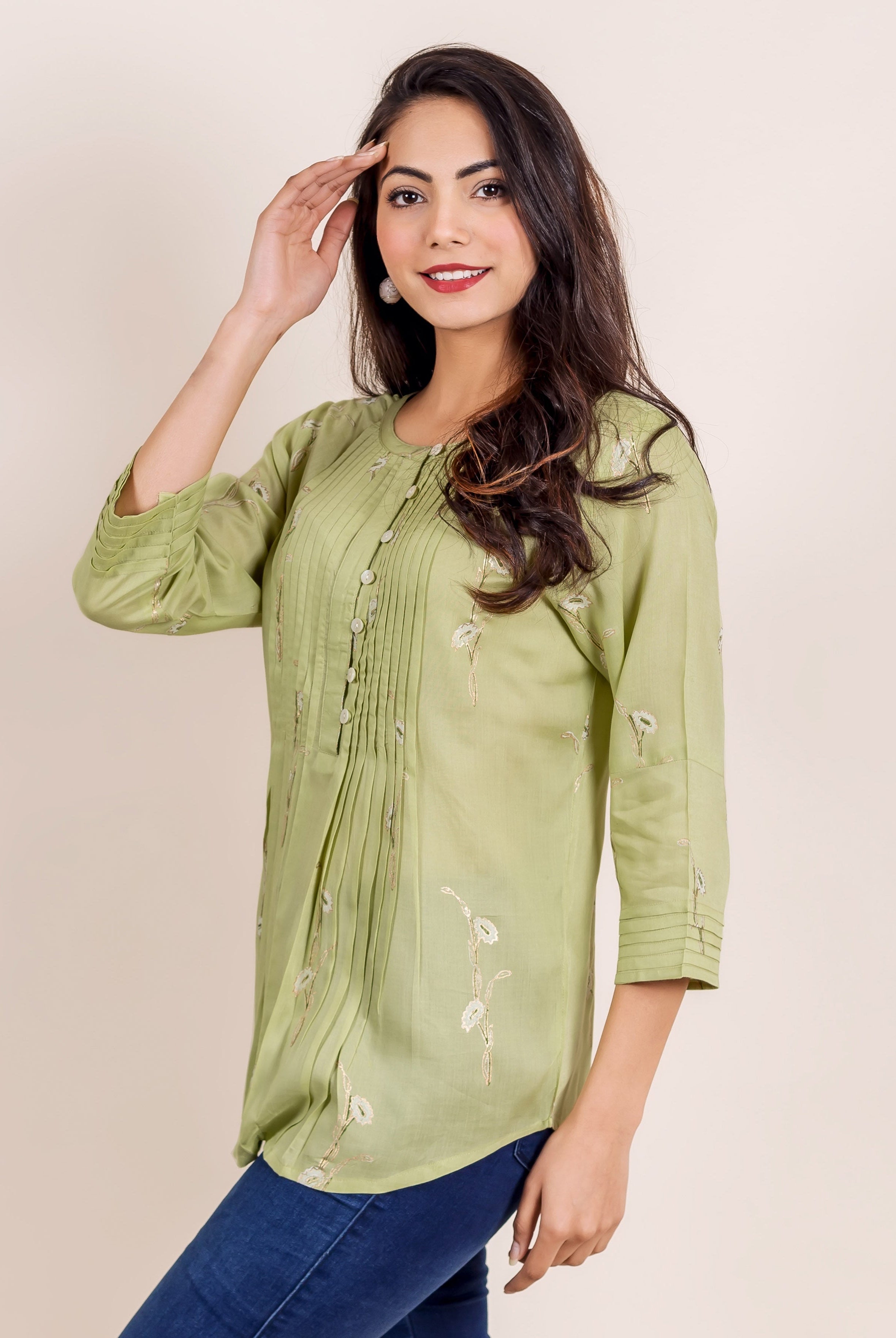 Smiling woman in a green hand block printed pleated top, three-quarter view.