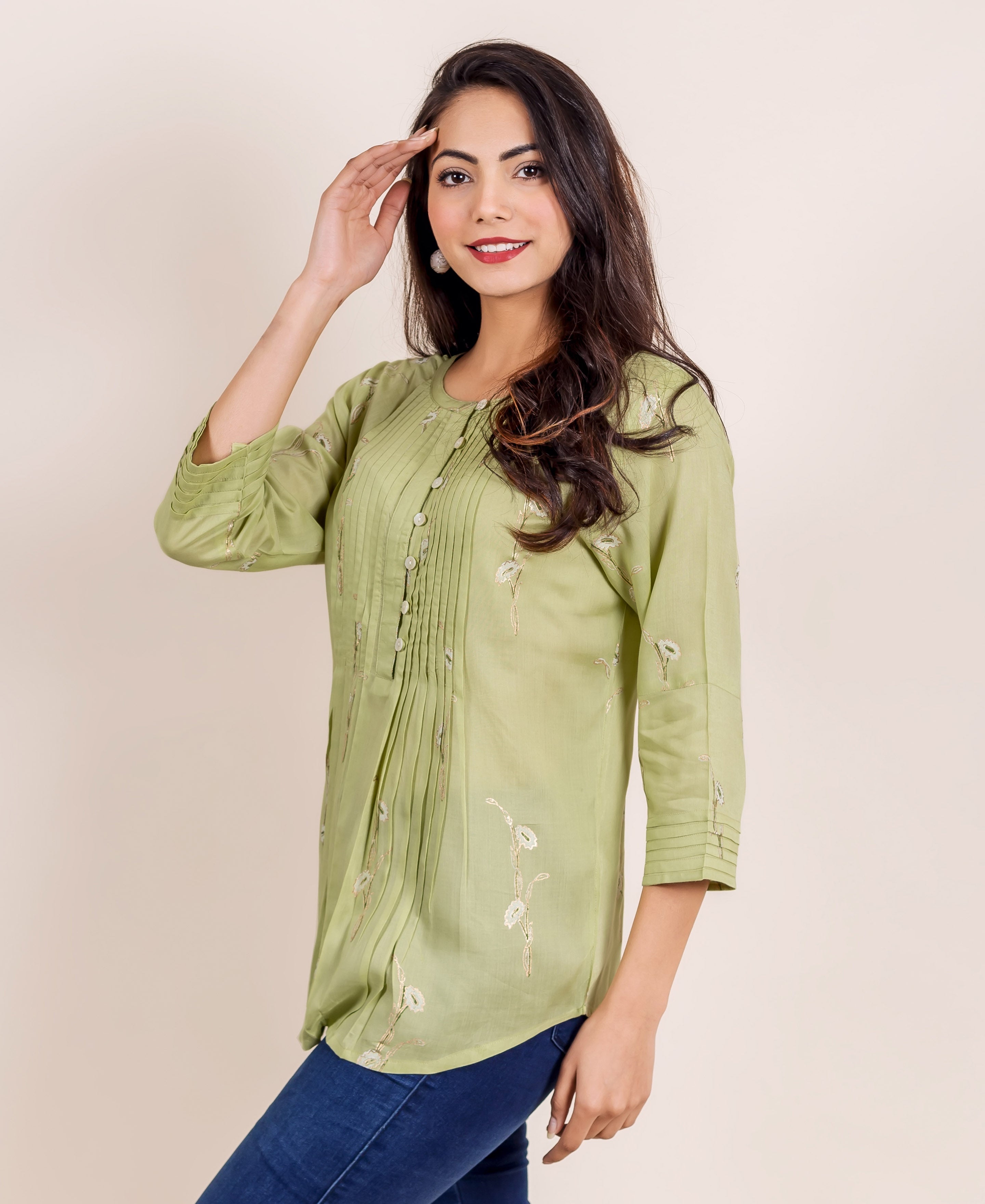 Smiling woman in a green hand block printed pleated top, three-quarter view.