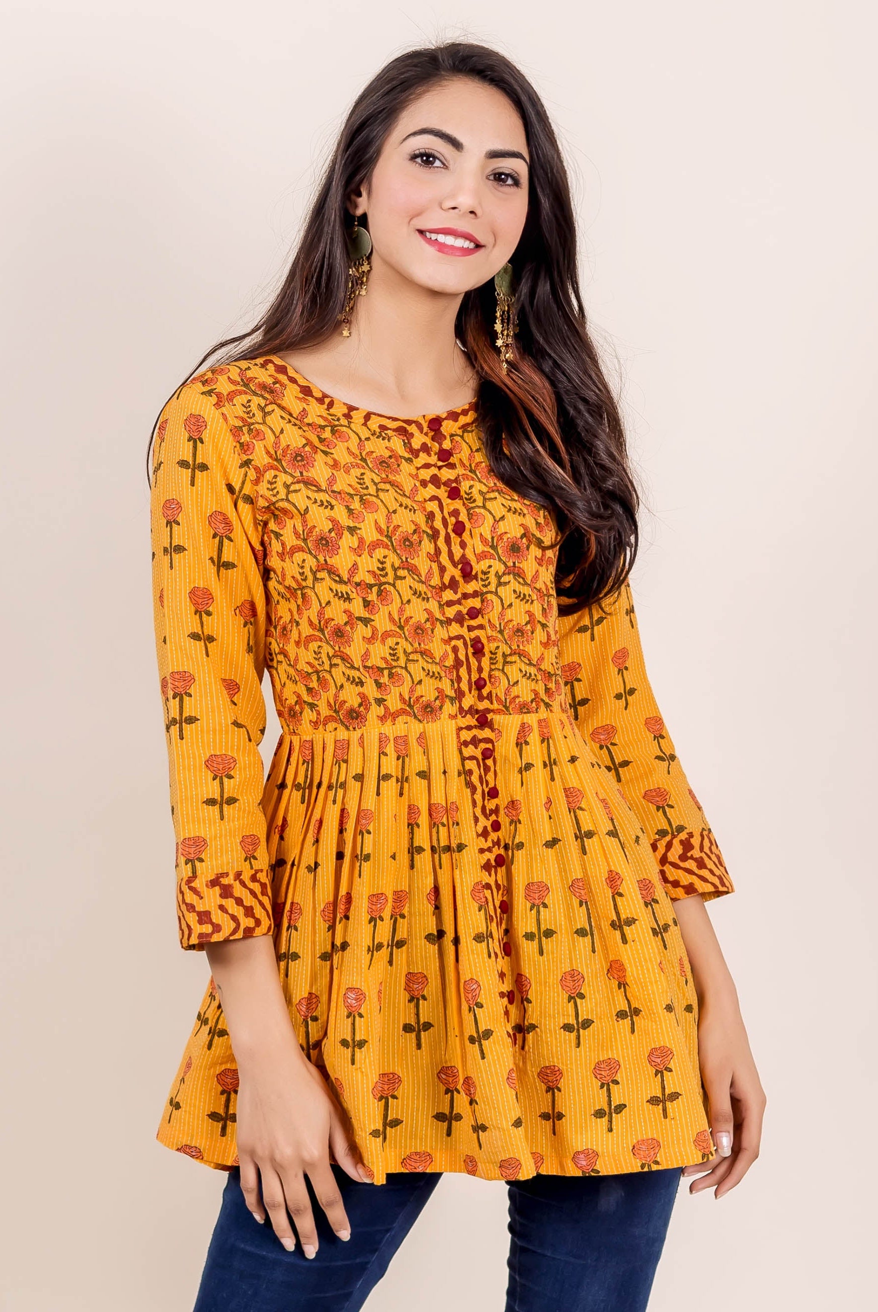 Smiling model in a yellow hand block printed peplum top with red floral patterns.