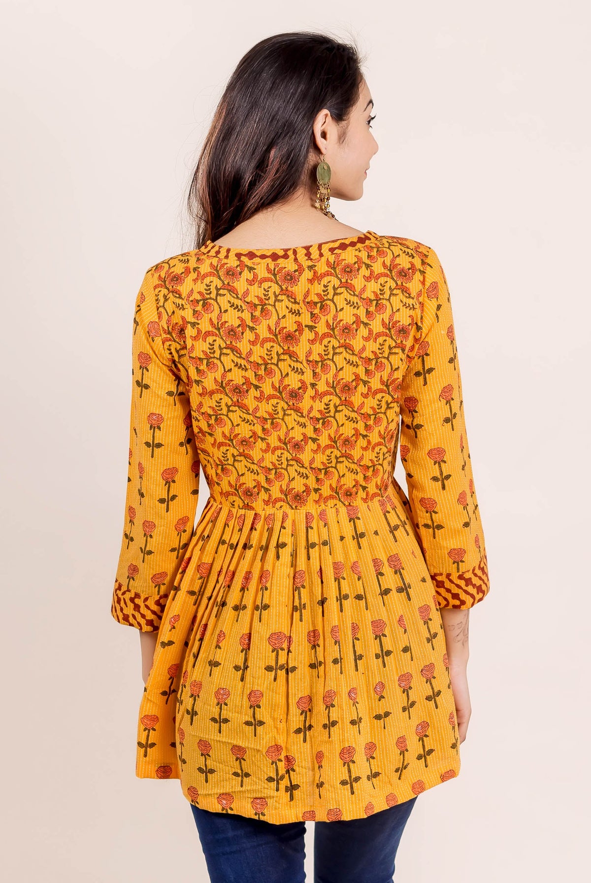 Rear view of model in yellow hand block printed peplum top with floral and rose print.