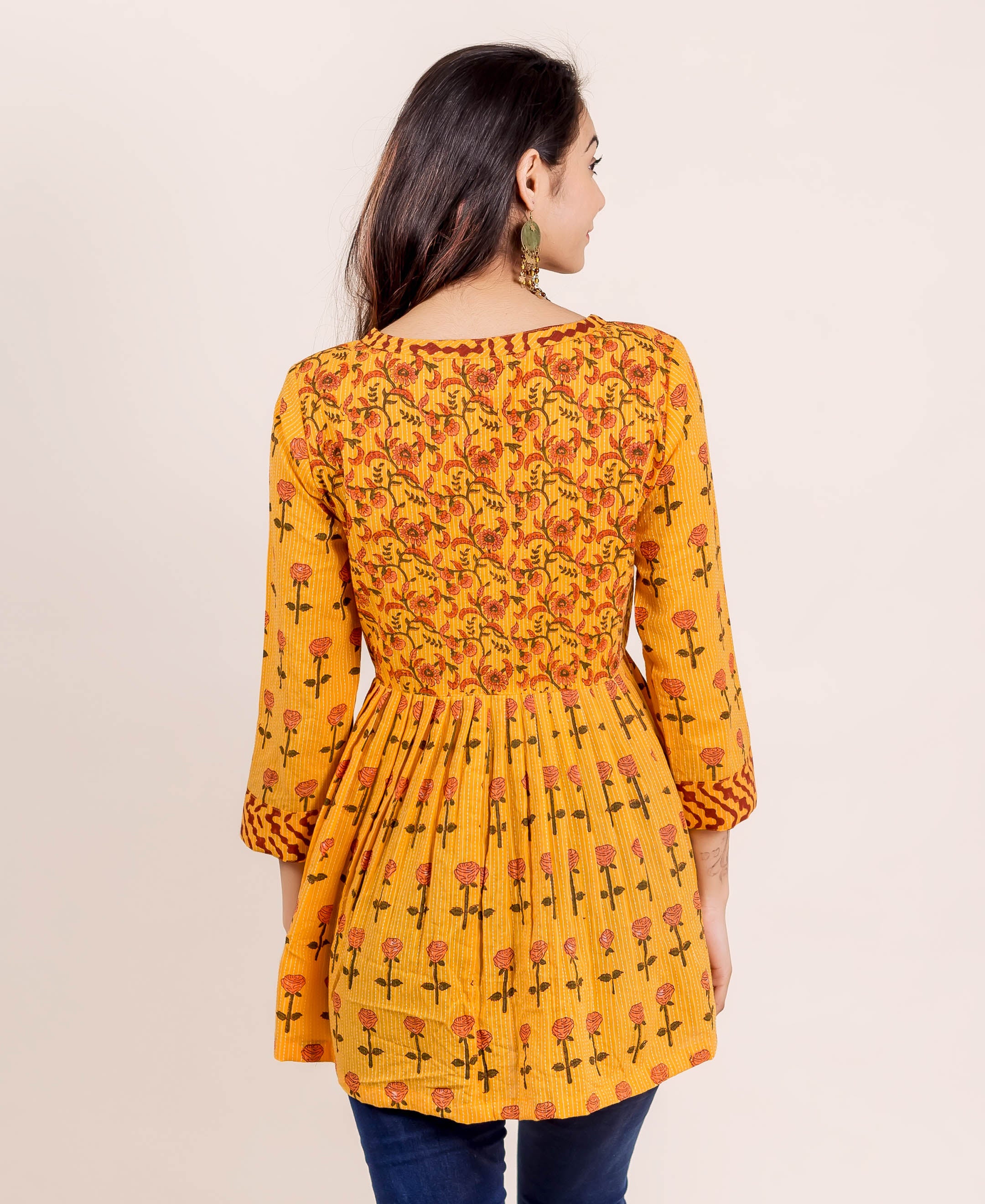 Rear view of model in yellow hand block printed peplum top with floral and rose print.