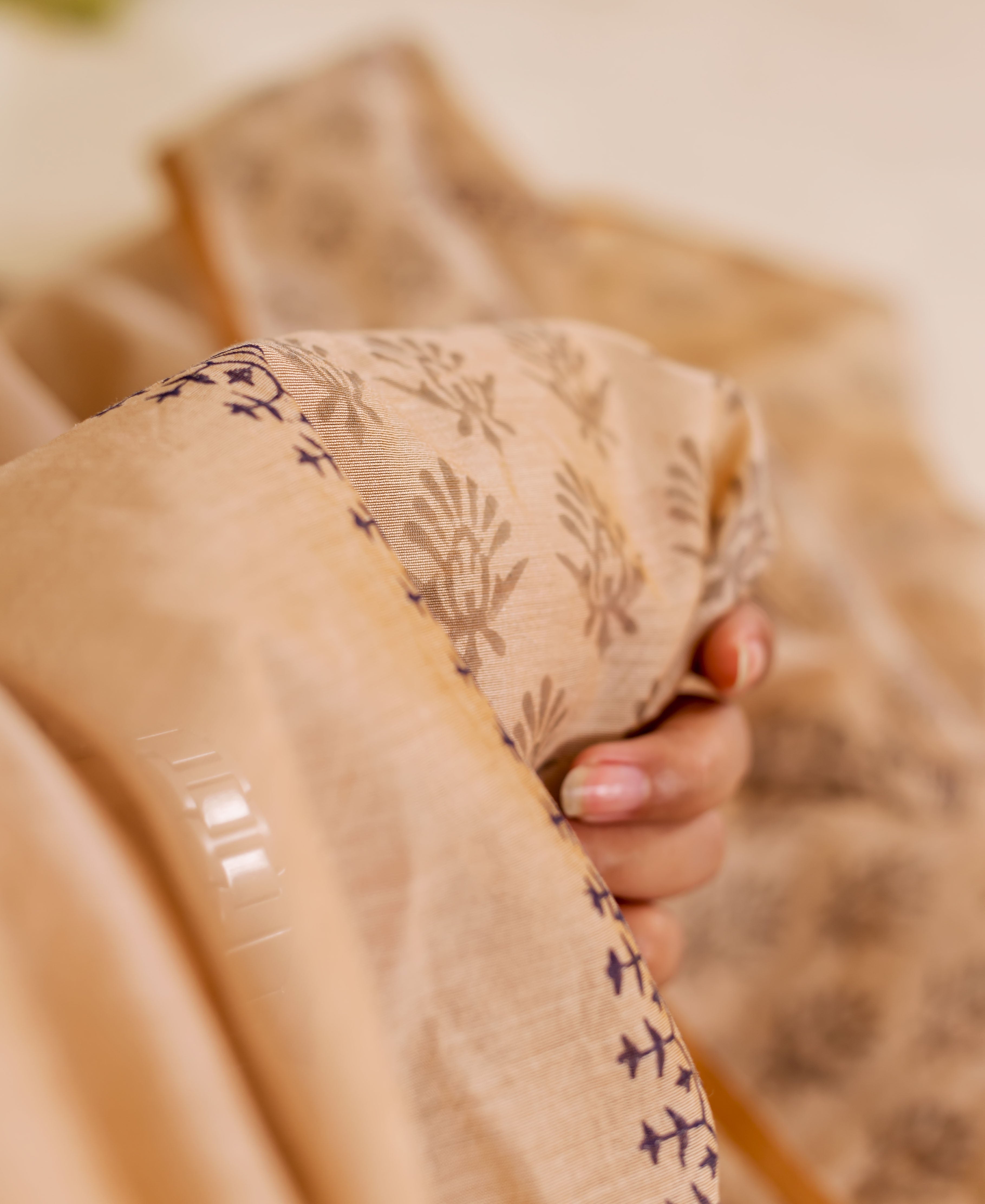 Close-up of a hand holding a beige chanderi dupatta with indigo block print leaf motifs.