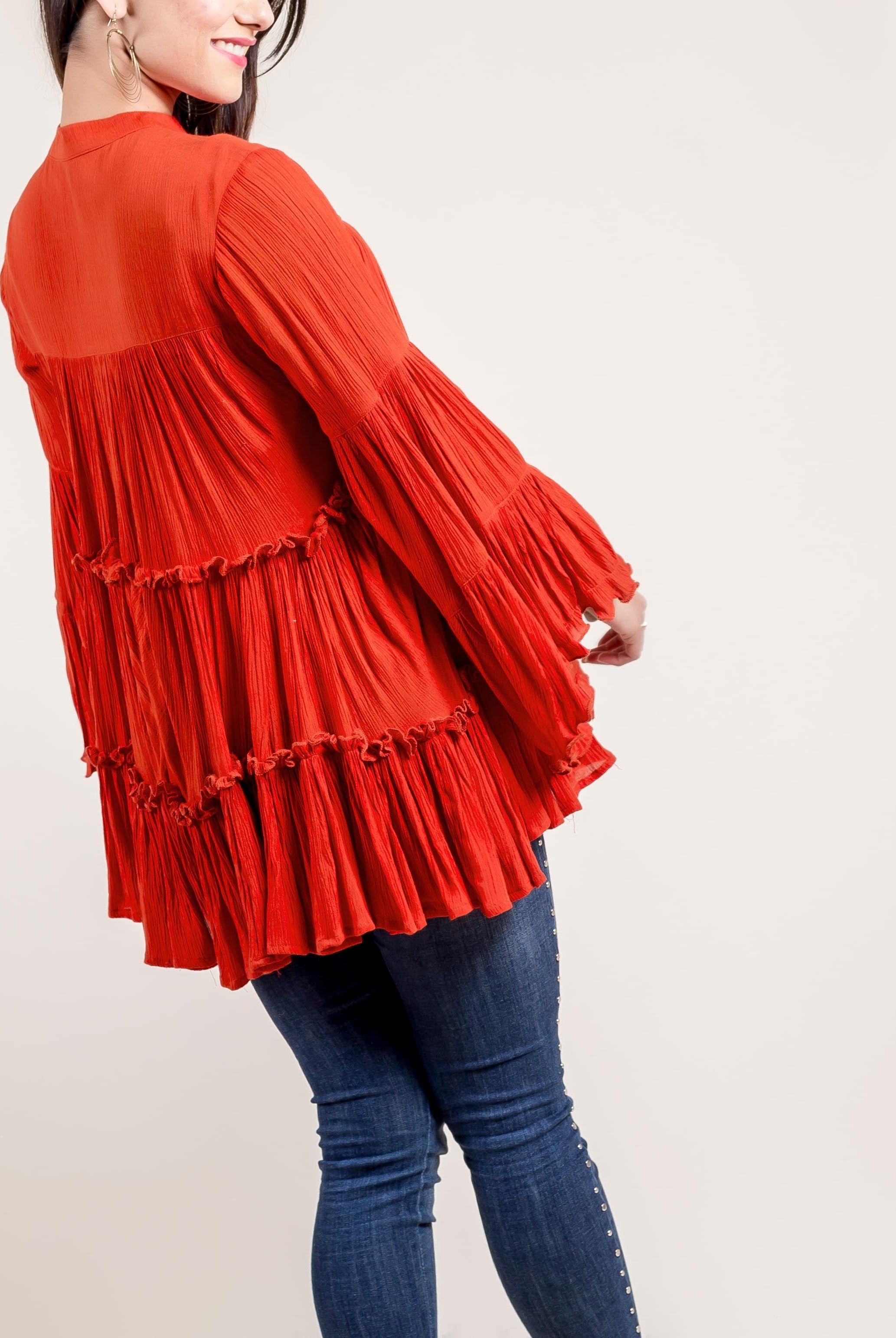 A model wearing a rust-colored, long-sleeved top with ruffles and tassels.