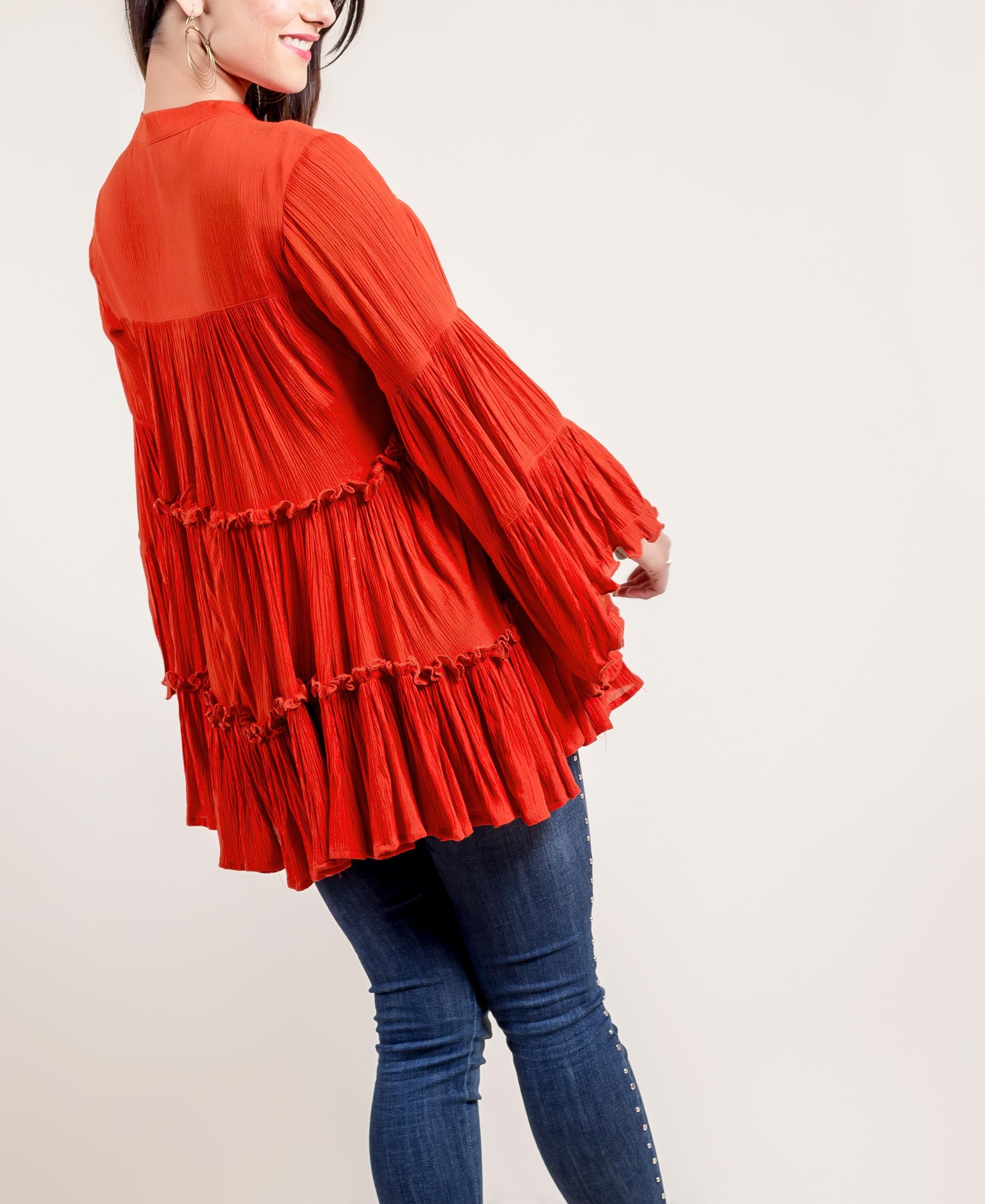 A model wearing a rust-colored, long-sleeved top with ruffles and tassels.