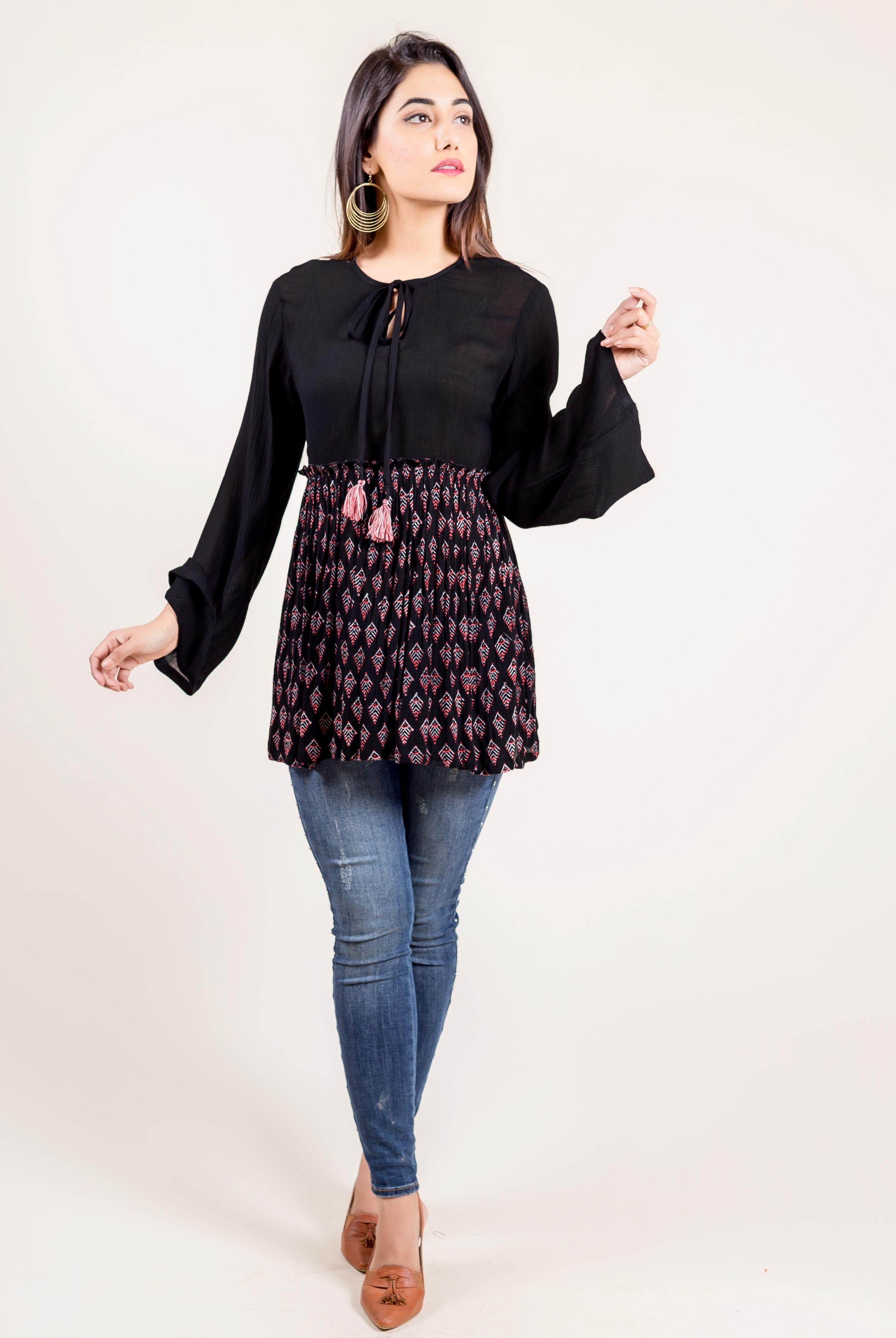 Front view of model wearing black bell-sleeve tunic with ethnic block print and blue jeans.