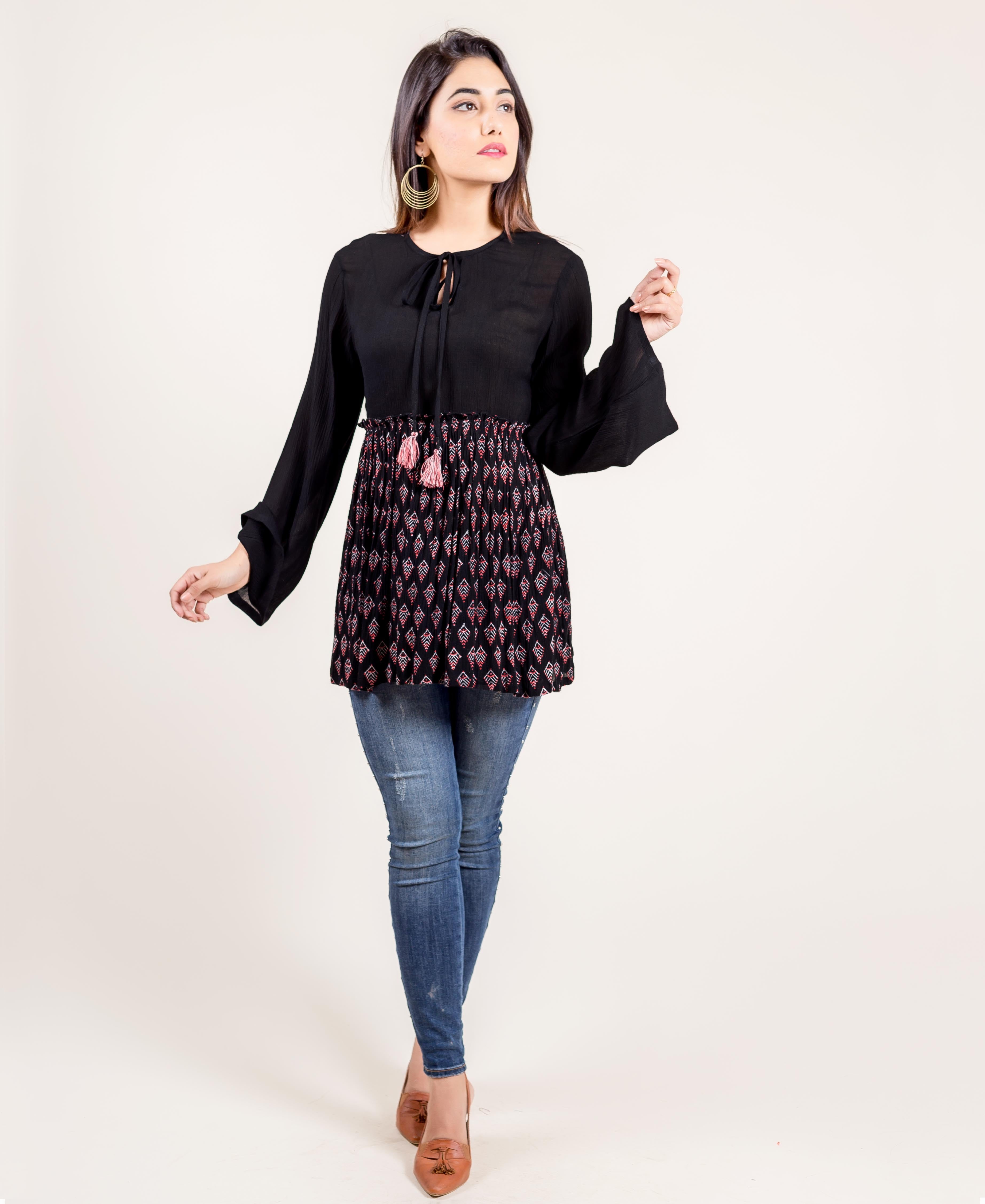 Front view of model wearing black bell-sleeve tunic with ethnic block print and blue jeans.