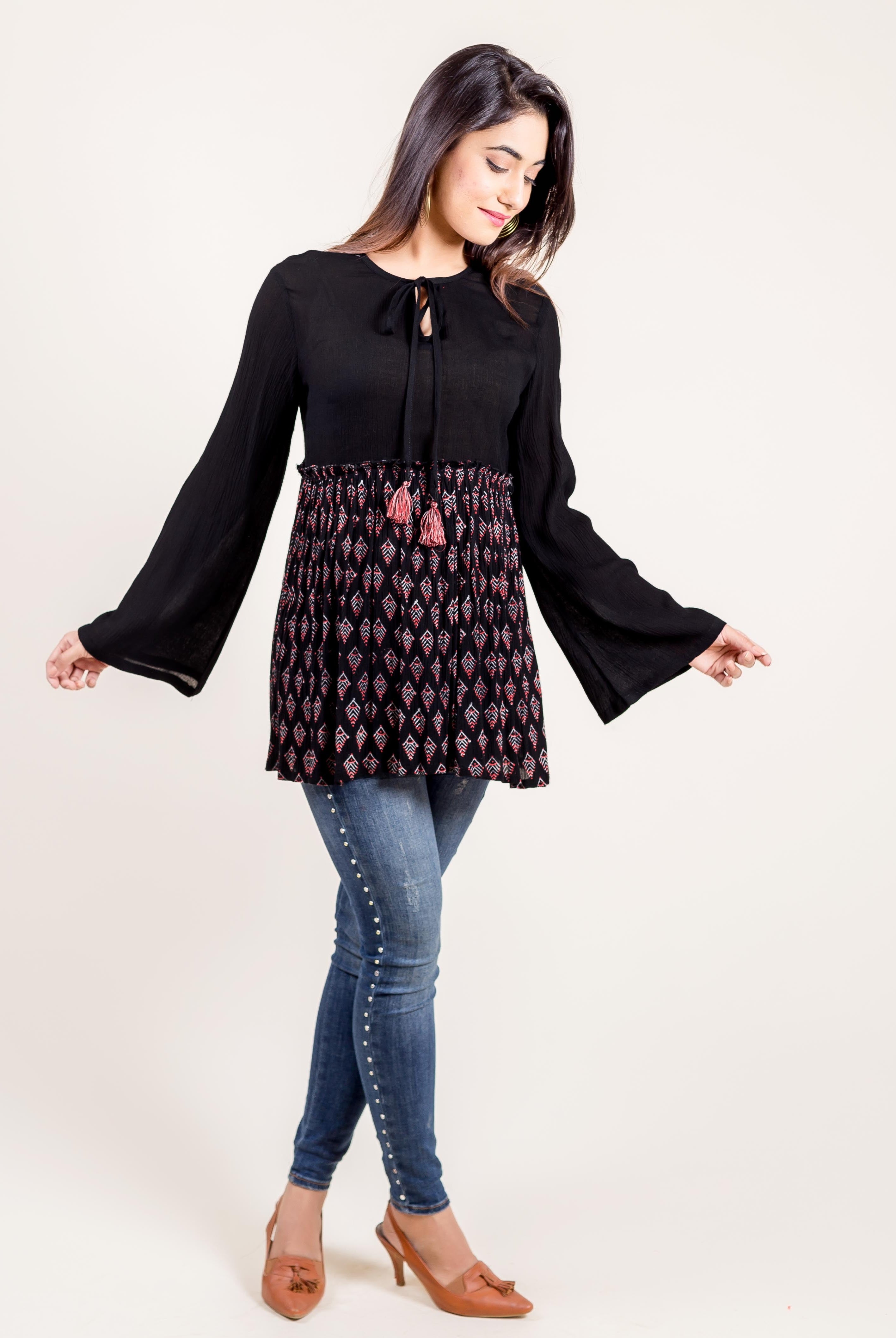 Front view of a model wearing a black tunic top with bell sleeves and a red/white ethnic block print.