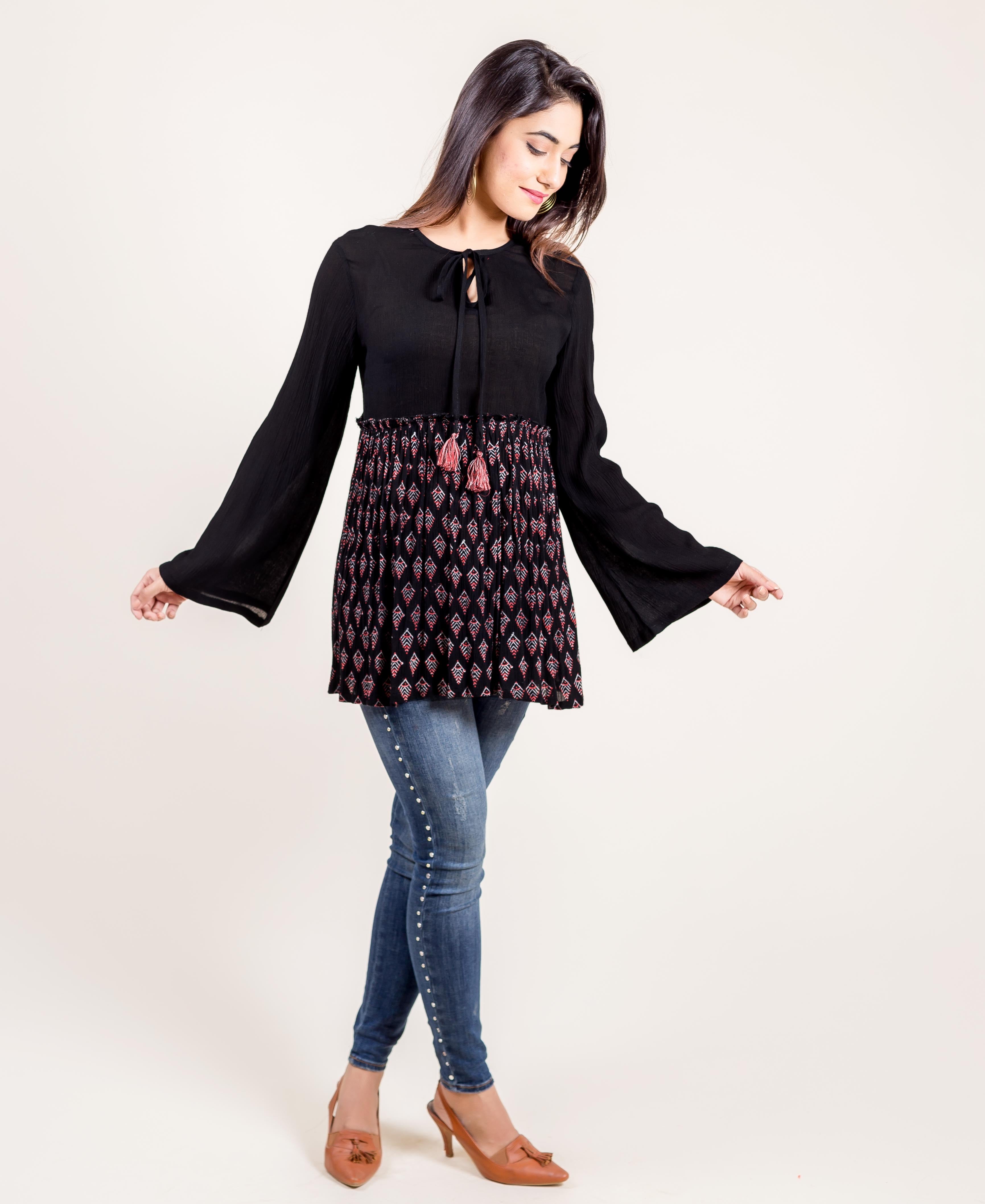 Front view of a model wearing a black tunic top with bell sleeves and a red/white ethnic block print.