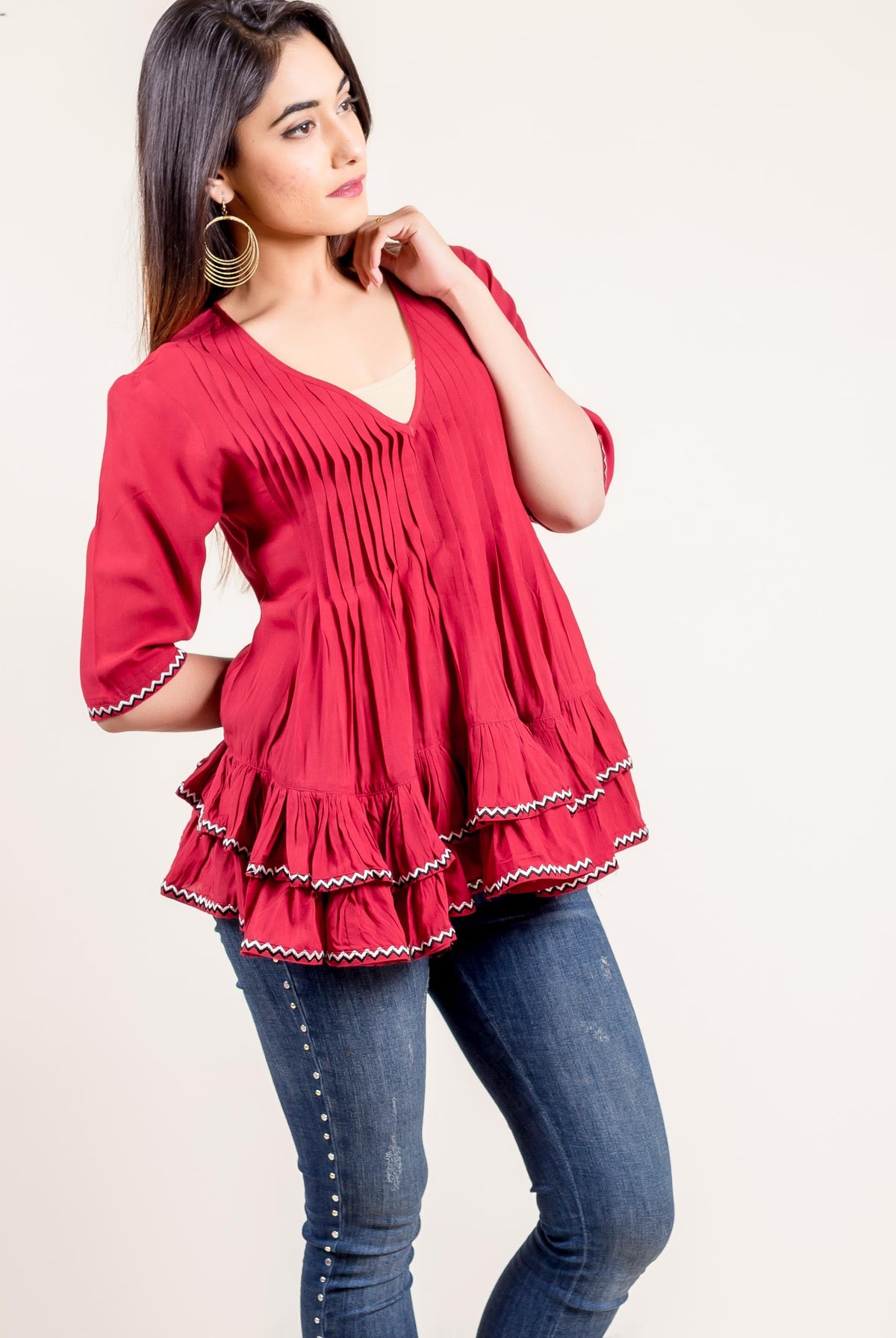 Model wears a vibrant red pleated frilled top with zigzag ethnic trim.