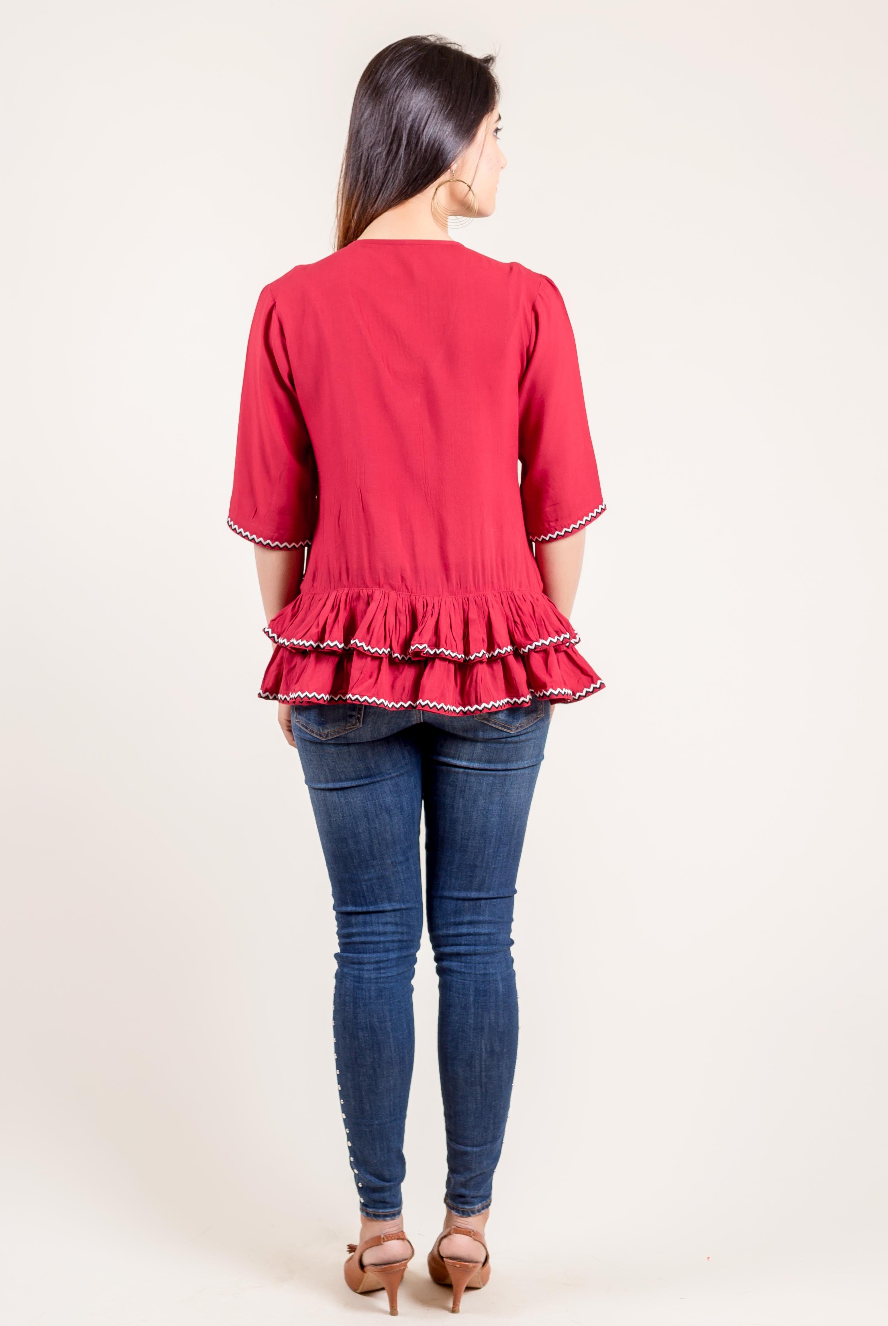 Back view of model in rust red frilled top with white zigzag trim and blue jeans.