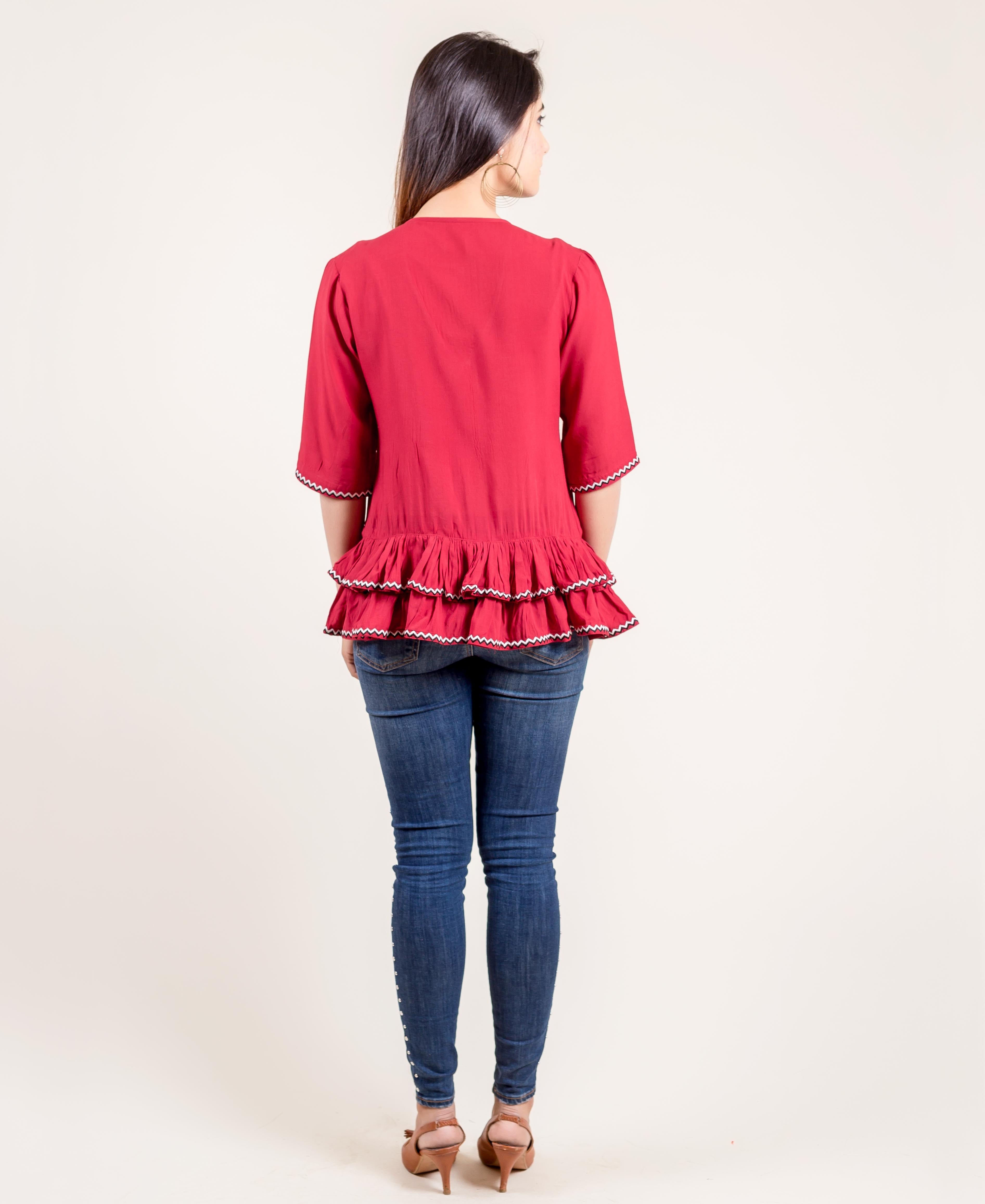Back view of model in rust red frilled top with white zigzag trim and blue jeans.