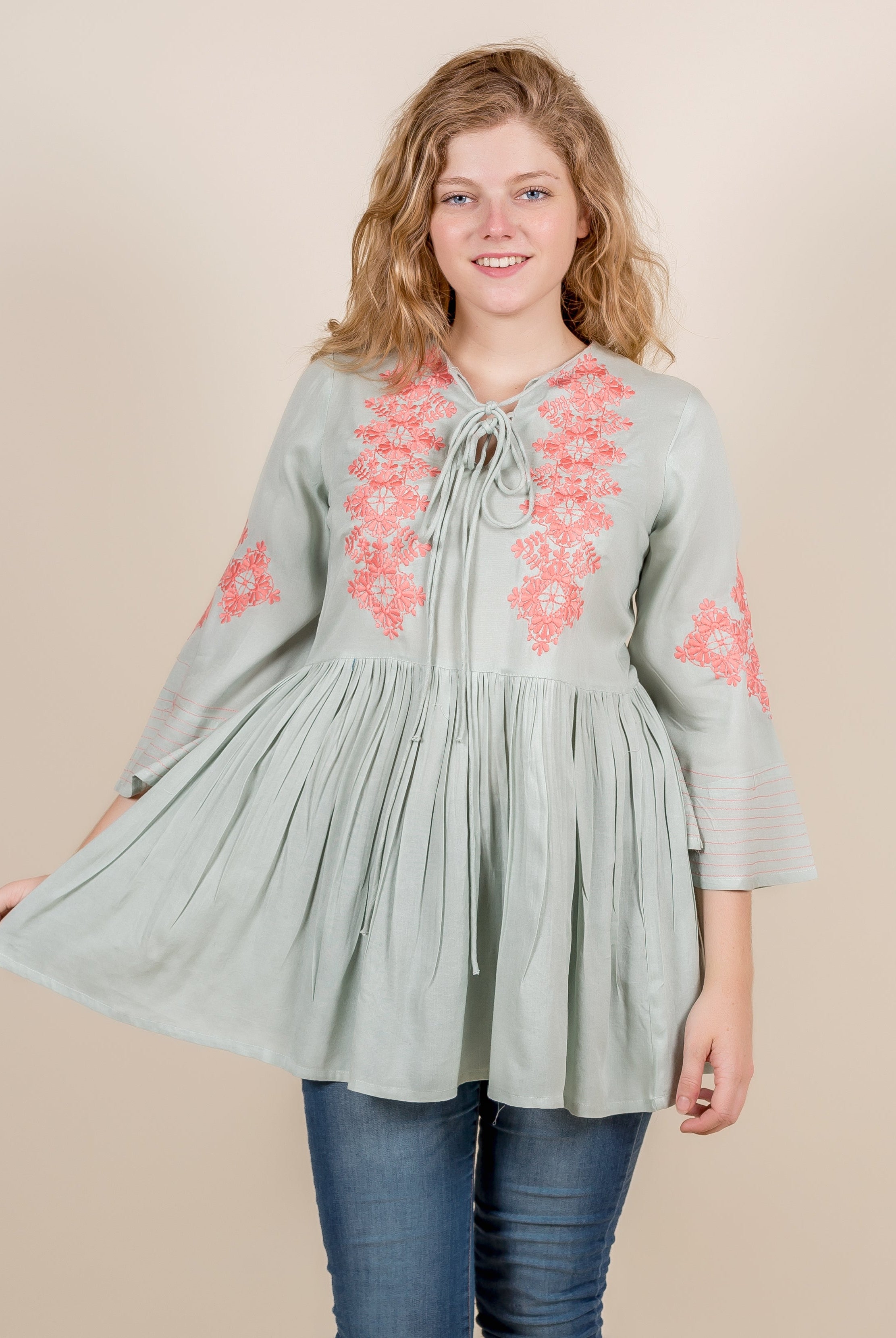Front view of a model wearing a mint green top with peach floral embroidery.