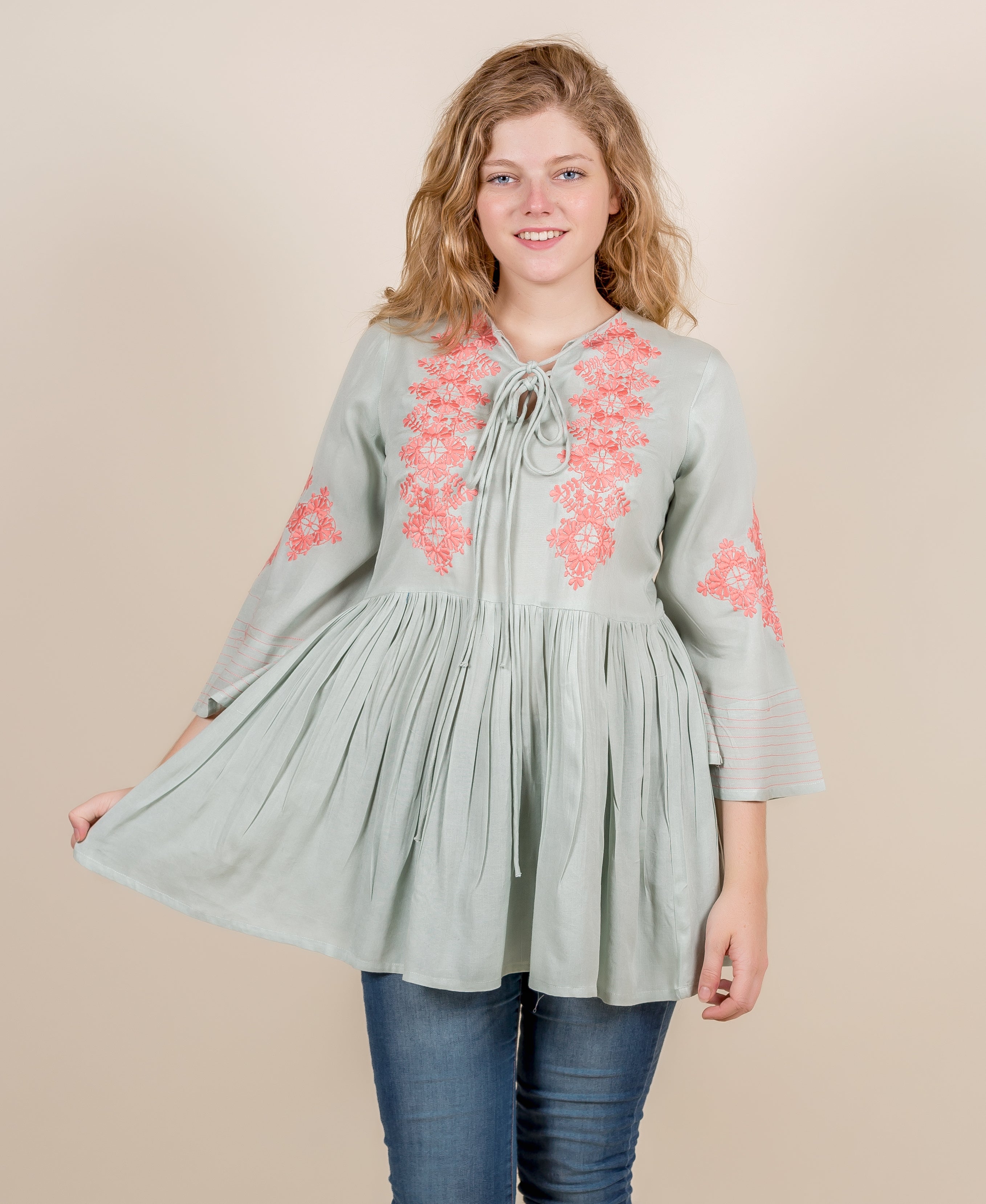 Front view of a model wearing a mint green top with peach floral embroidery.