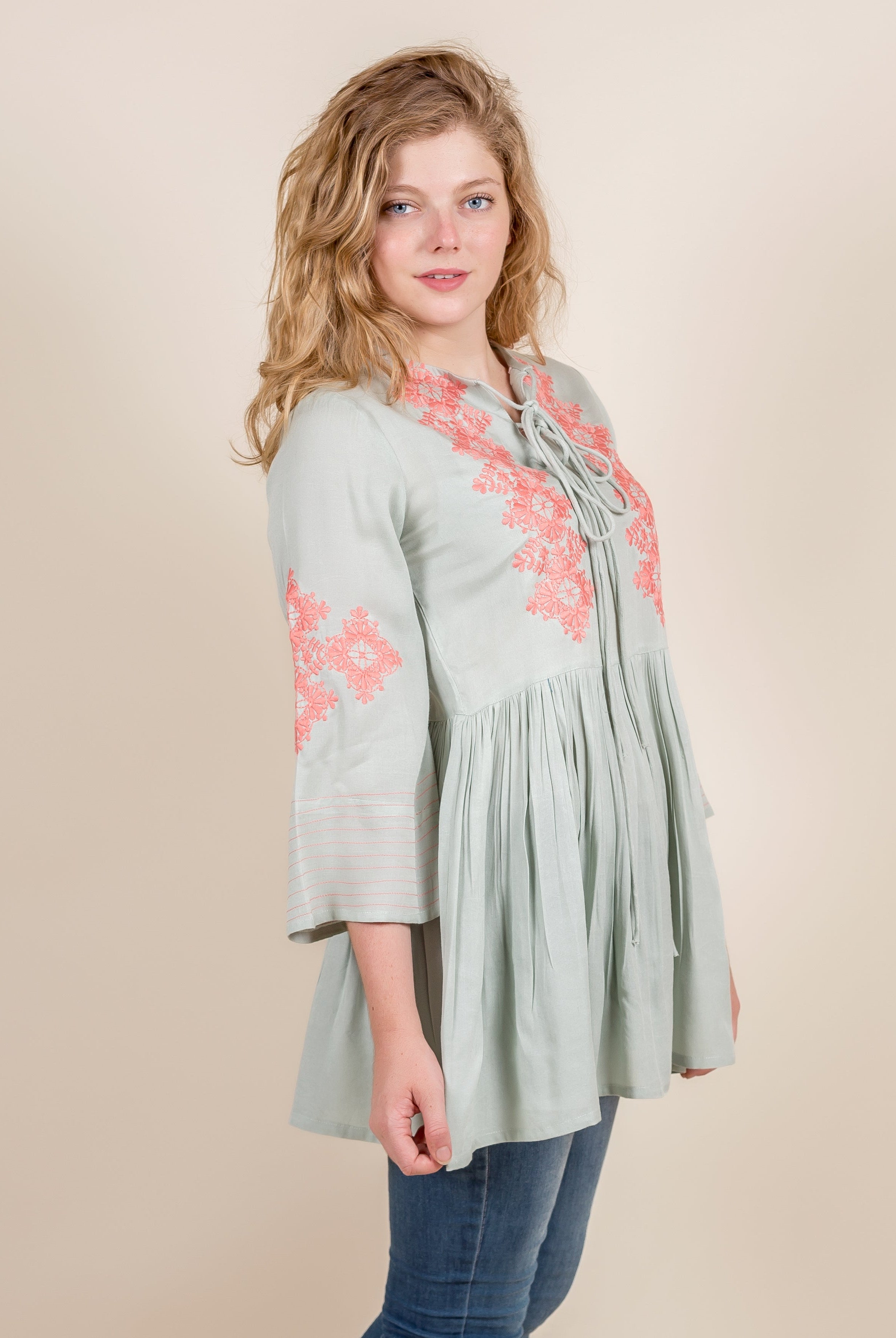 Front view of model wearing a mint green ethnic top with peach embroidery and pleated body.