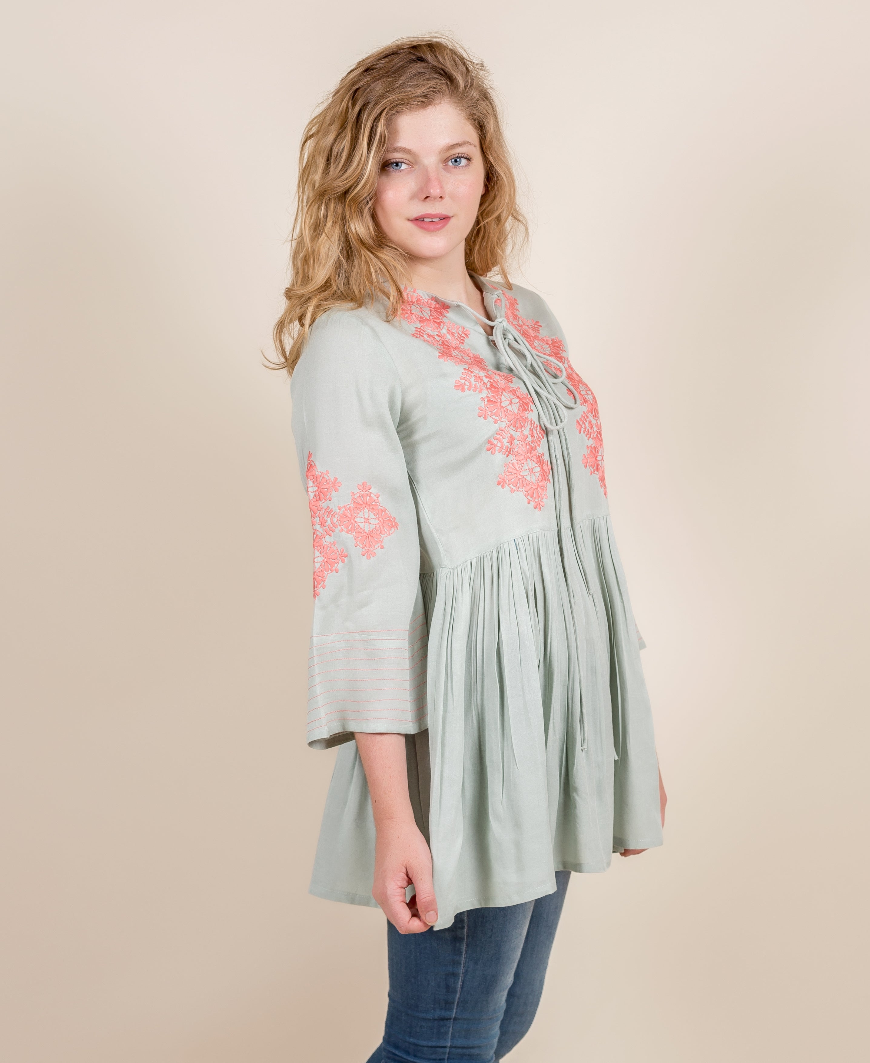 Front view of model wearing a mint green ethnic top with peach embroidery and pleated body.