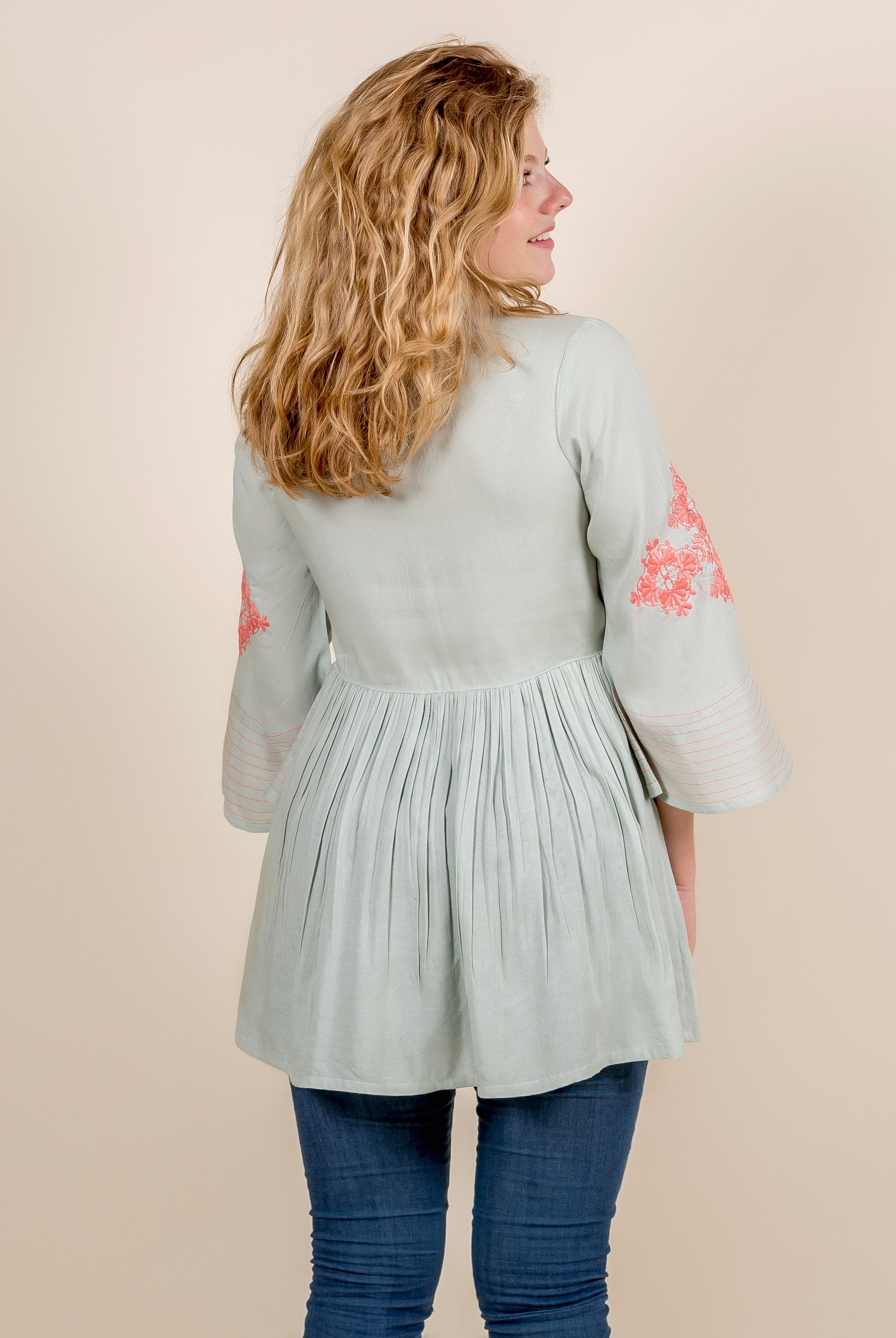 Back view of model in mint green top with pleated waist and peach embroidered sleeves.