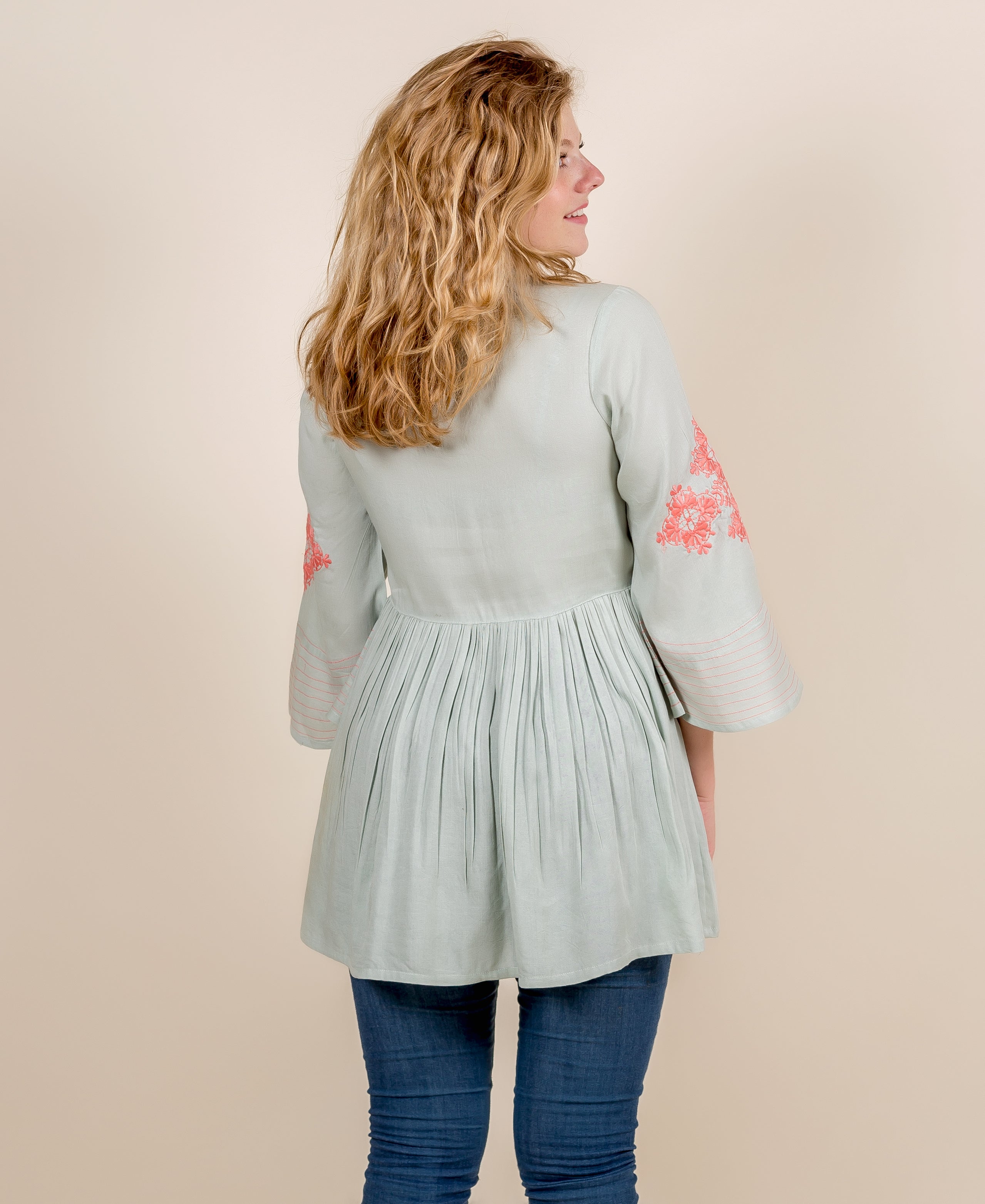 Back view of model in mint green top with pleated waist and peach embroidered sleeves.