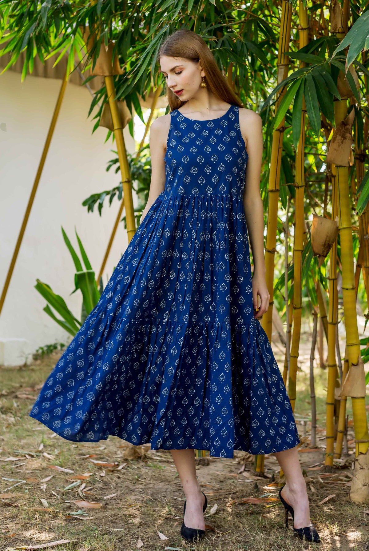Woman wearing an indigo blue sleeveless tiered dress with white hand block prints.